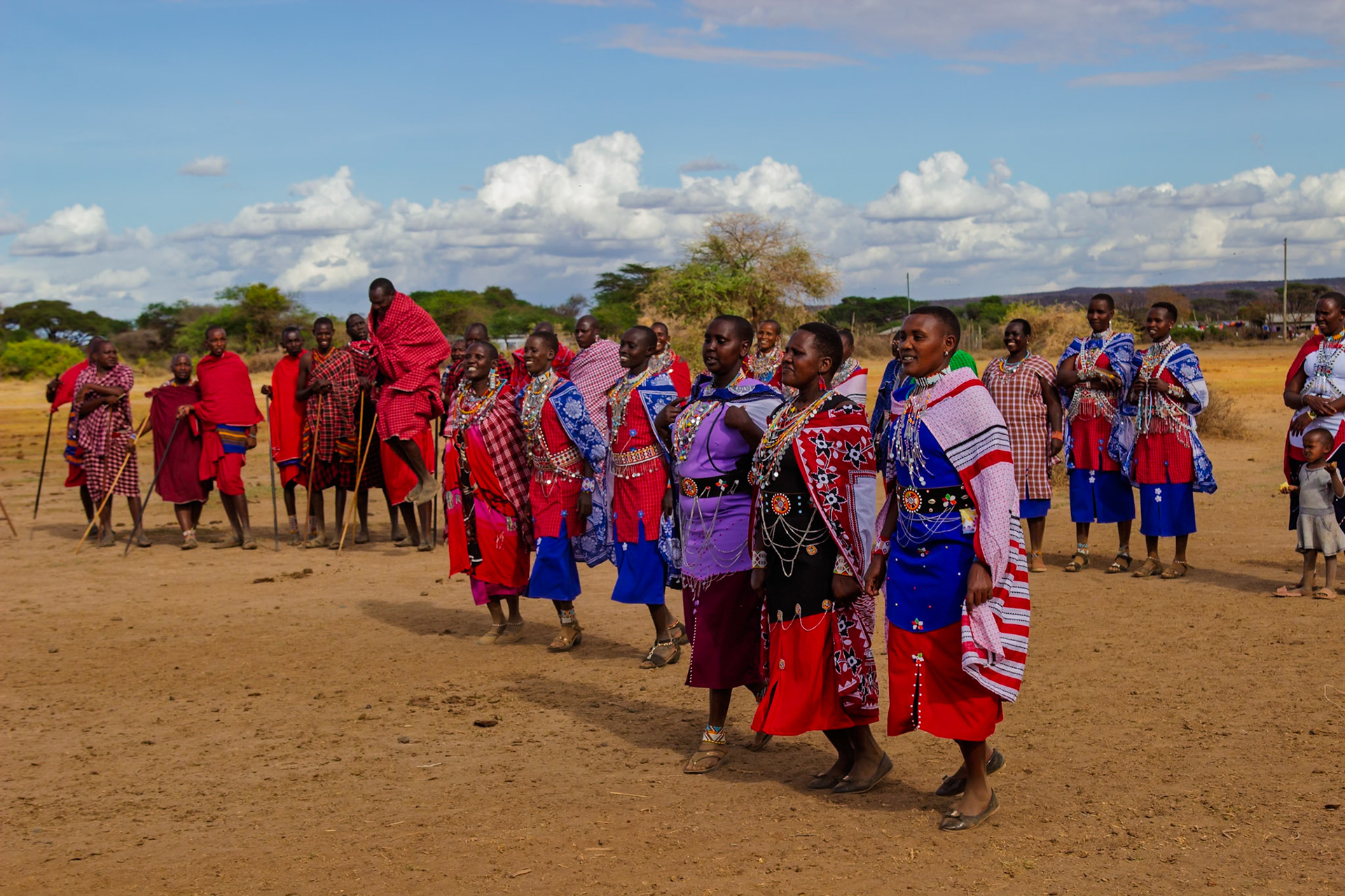 Maasai men leap while women walk in a line, adorned in colorful traditional clothing, during a ceremony in their Kenyan village.