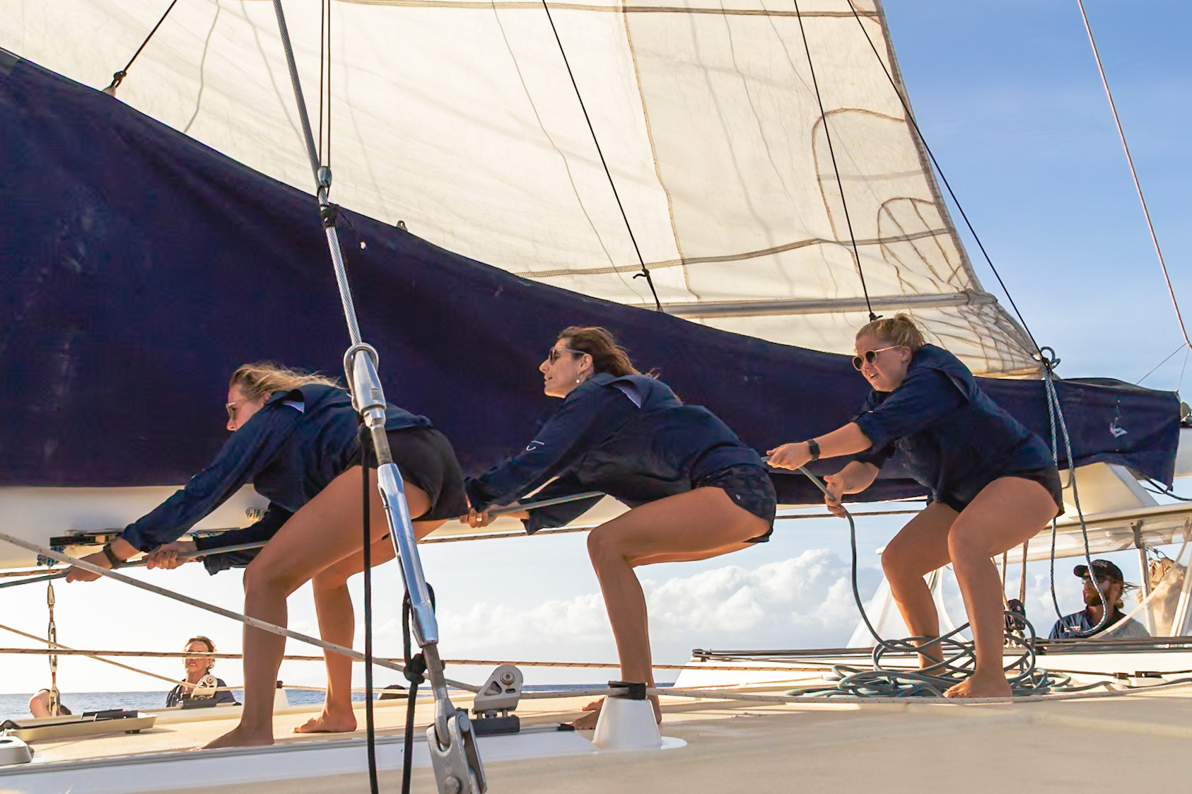 Maui, Hawaii, USA - April 7th 2022: Three women are pulling a rope on a sailboat, likely adjusting the sail for optimal wind capture.