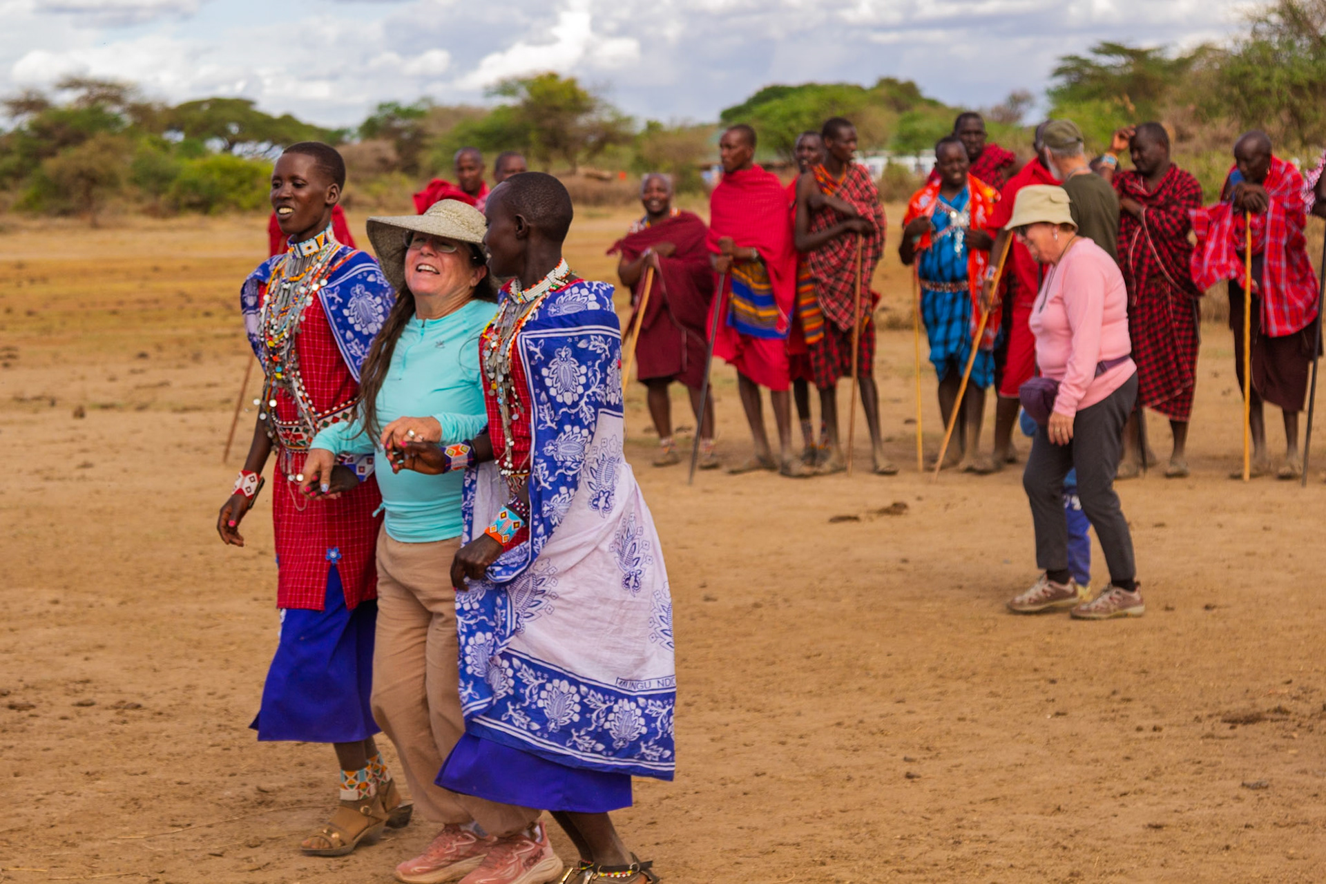 Tourists visit a Maasai village in Kenya, experiencing local culture by dancing with Maasai people in traditional clothing.