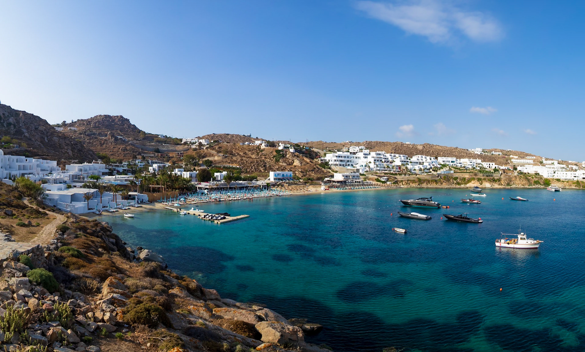 Psarou Beach, Mykonos, Greece - May 24th 2018: A scenic view of the beach, boats, and buildings on a sunny day, showcasing the island's beauty.