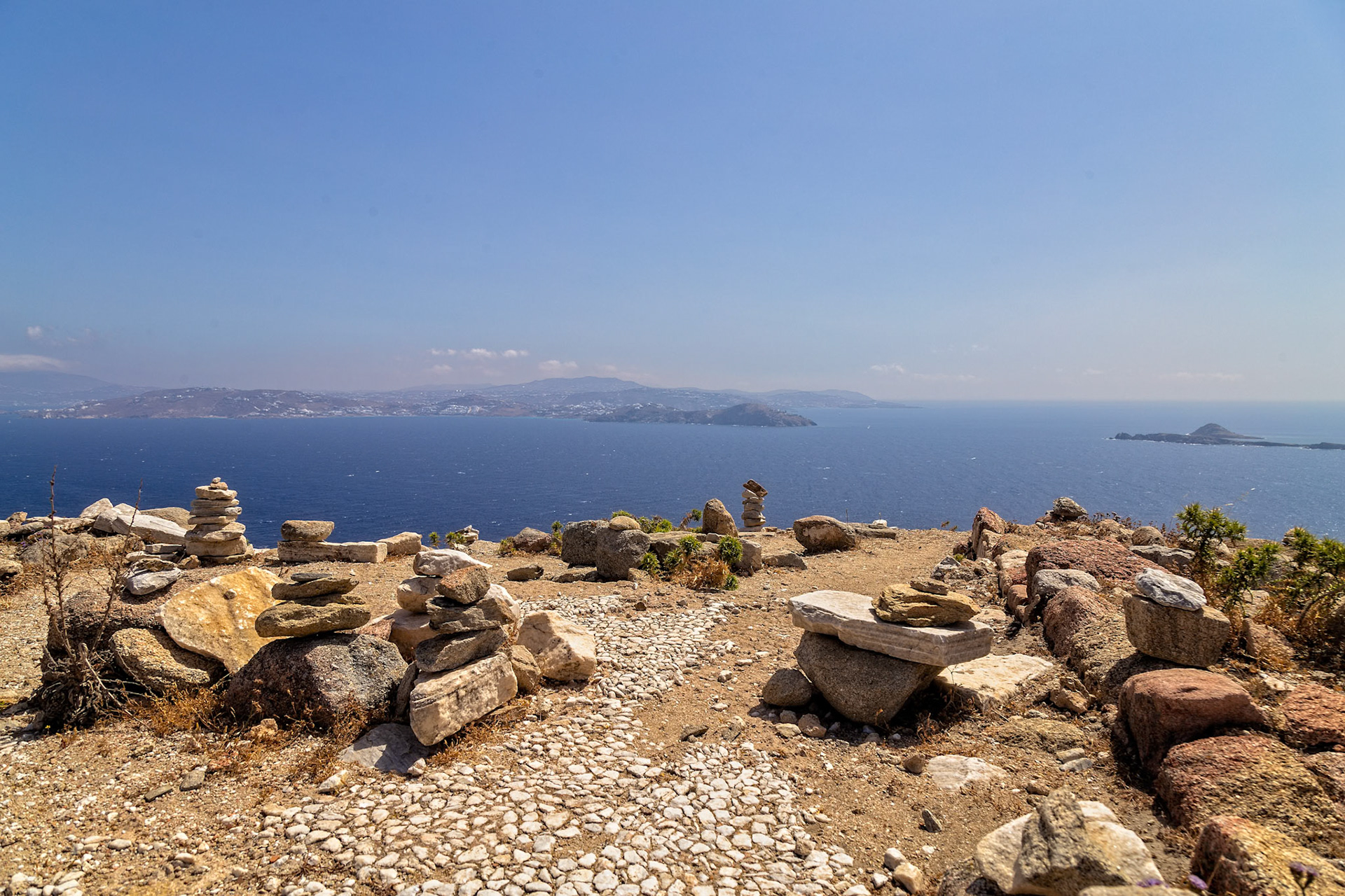 Delos, Greece - May 22nd 2018: Rock cairns stand on a hill overlooking the Aegean Sea. These structures are built by visitors to mark their journey and experience.
