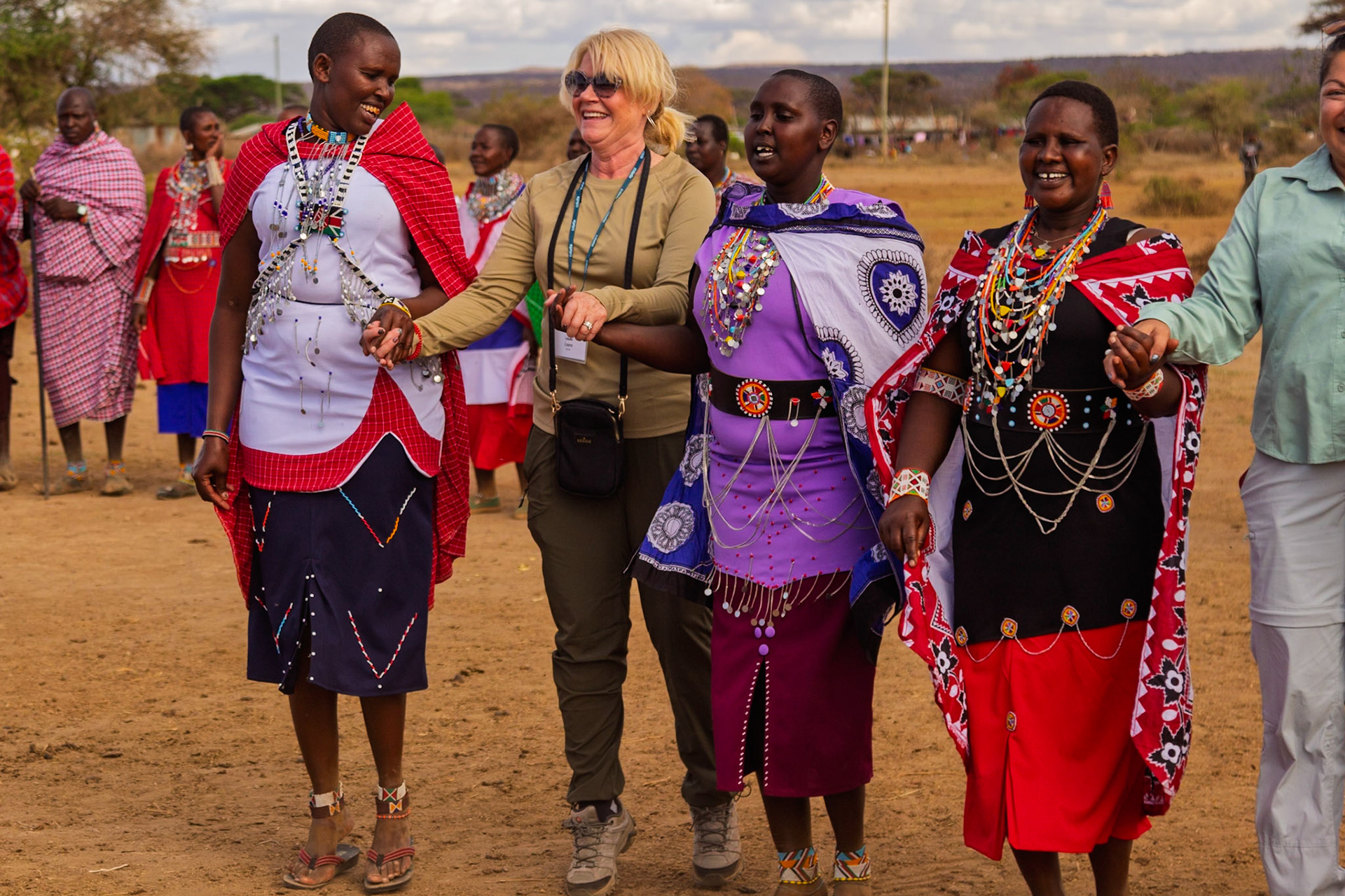 A tourist visits a Maasai village in Kenya, holding hands with Maasai women in traditional dress, sharing a cultural experience.