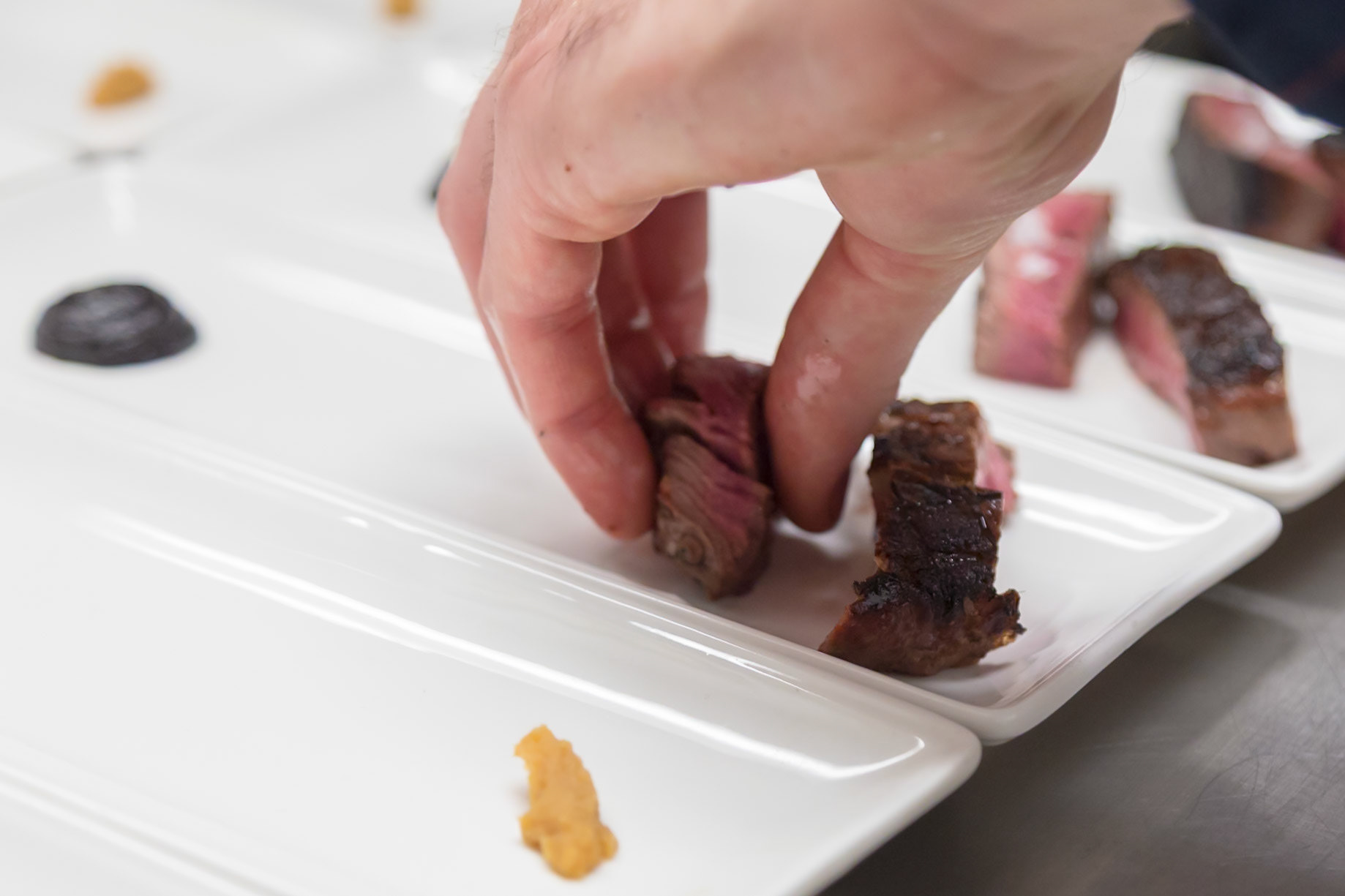 Fog Lark, Portland, Oregon - April 6th 2018: A chef plates sliced steak with sauces, preparing individual servings for a tasting menu.