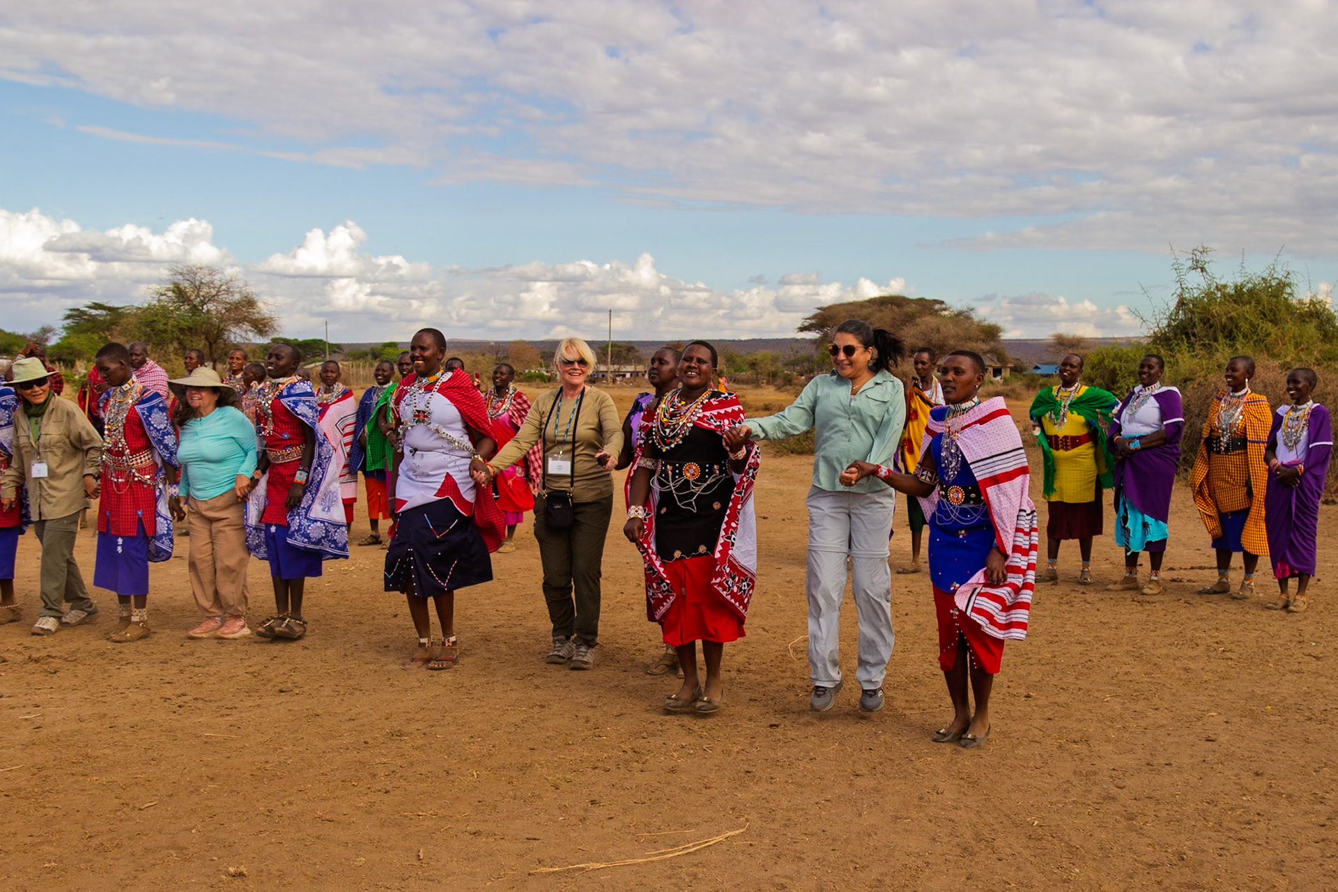 Tourists join Maasai women in a traditional dance in a village in Kenya, experiencing local culture.