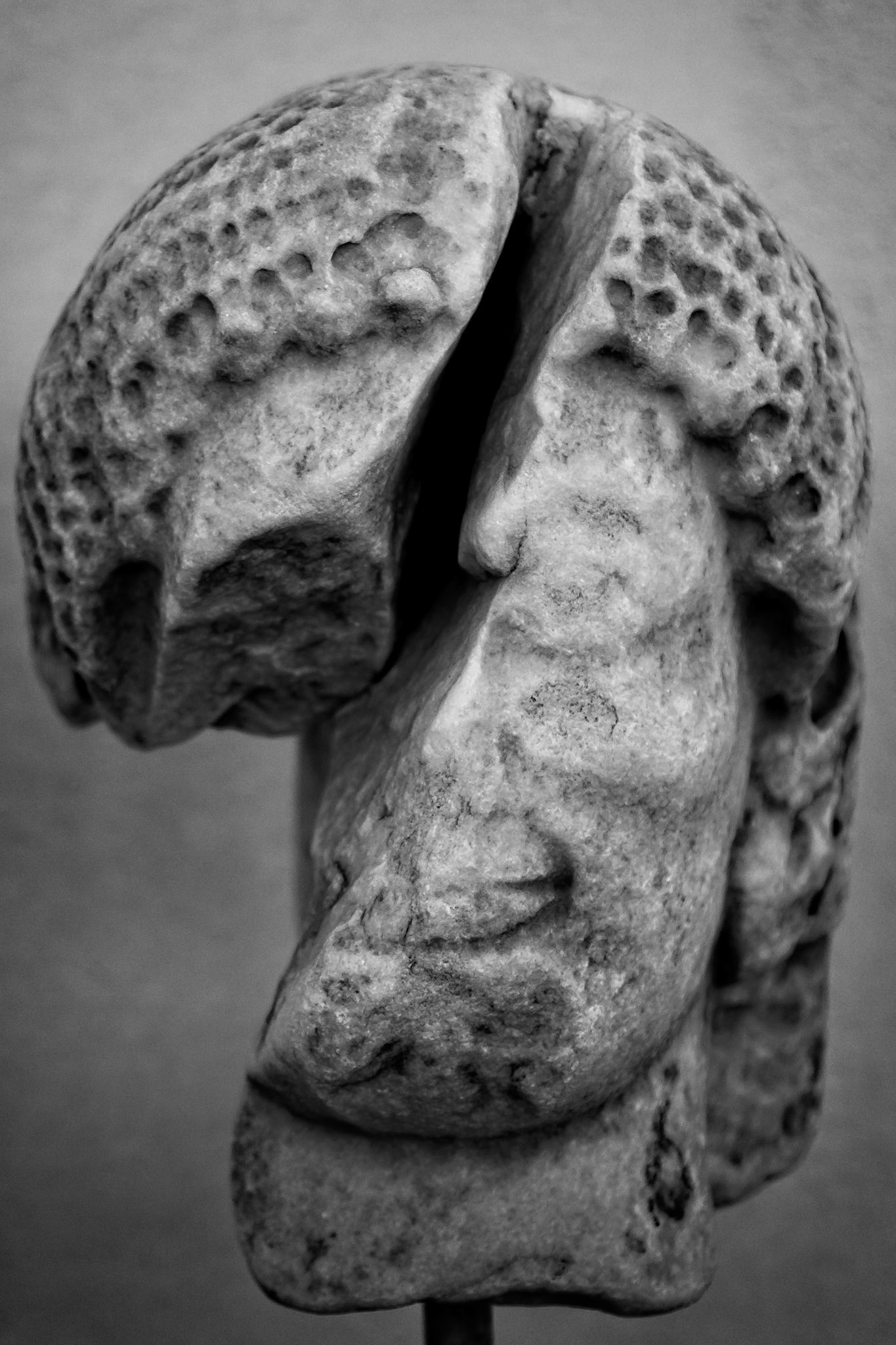 Delos, Greece - May 22nd 2018: A weathered marble head sculpture is displayed. The statue's face is visible, with a damaged cranium, showcasing the effects of time.