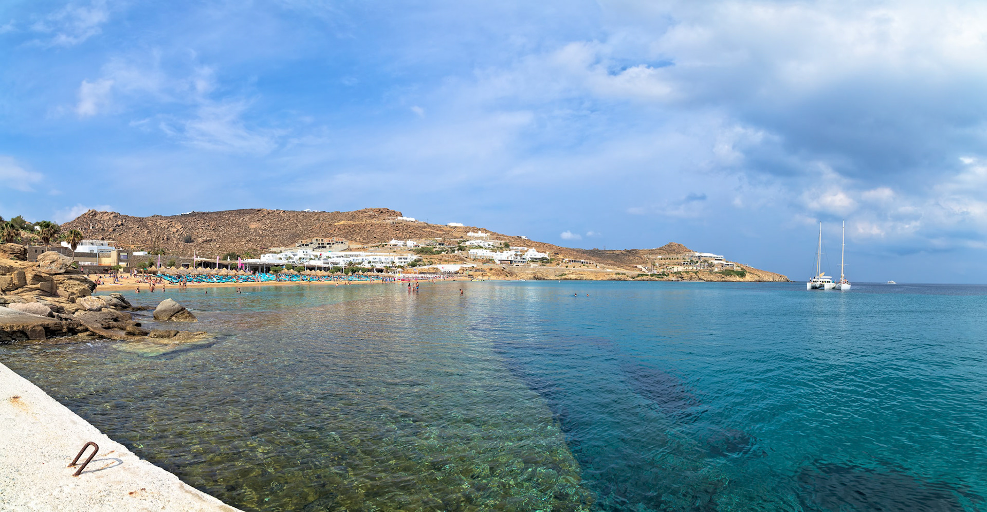 Paradise Beach, Mykonos, Greece - May 24th 2018: People enjoy the sun and sea at Paradise Beach, with yachts anchored offshore.