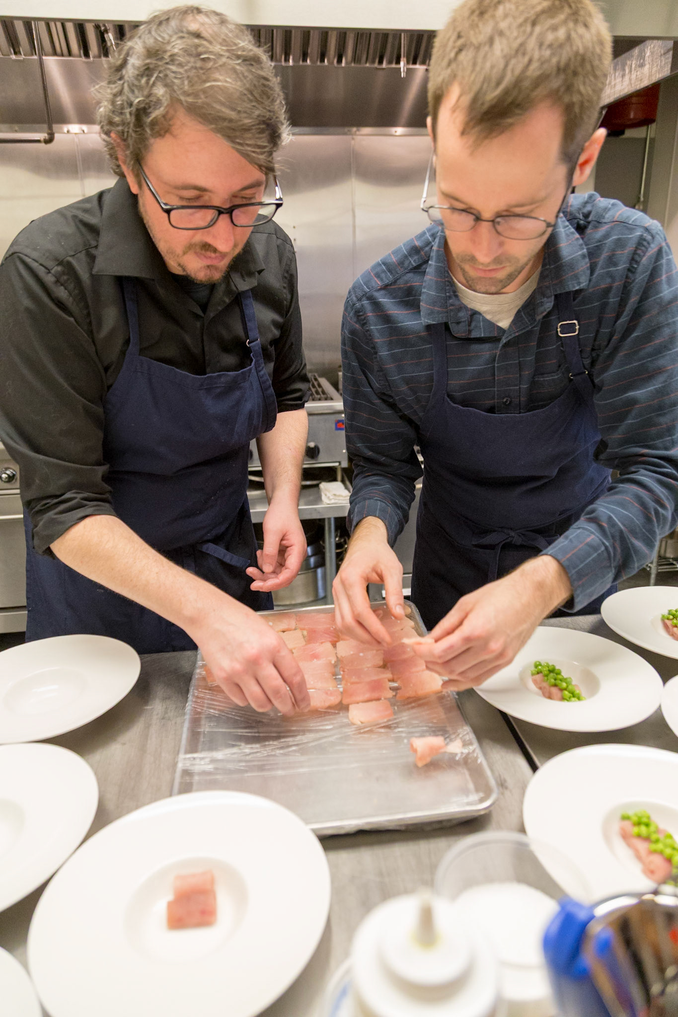 Fog Lark, Portland, Oregon - April 6th 2018: Two chefs in aprons meticulously plate a dish with tuna and peas in a professional kitchen.