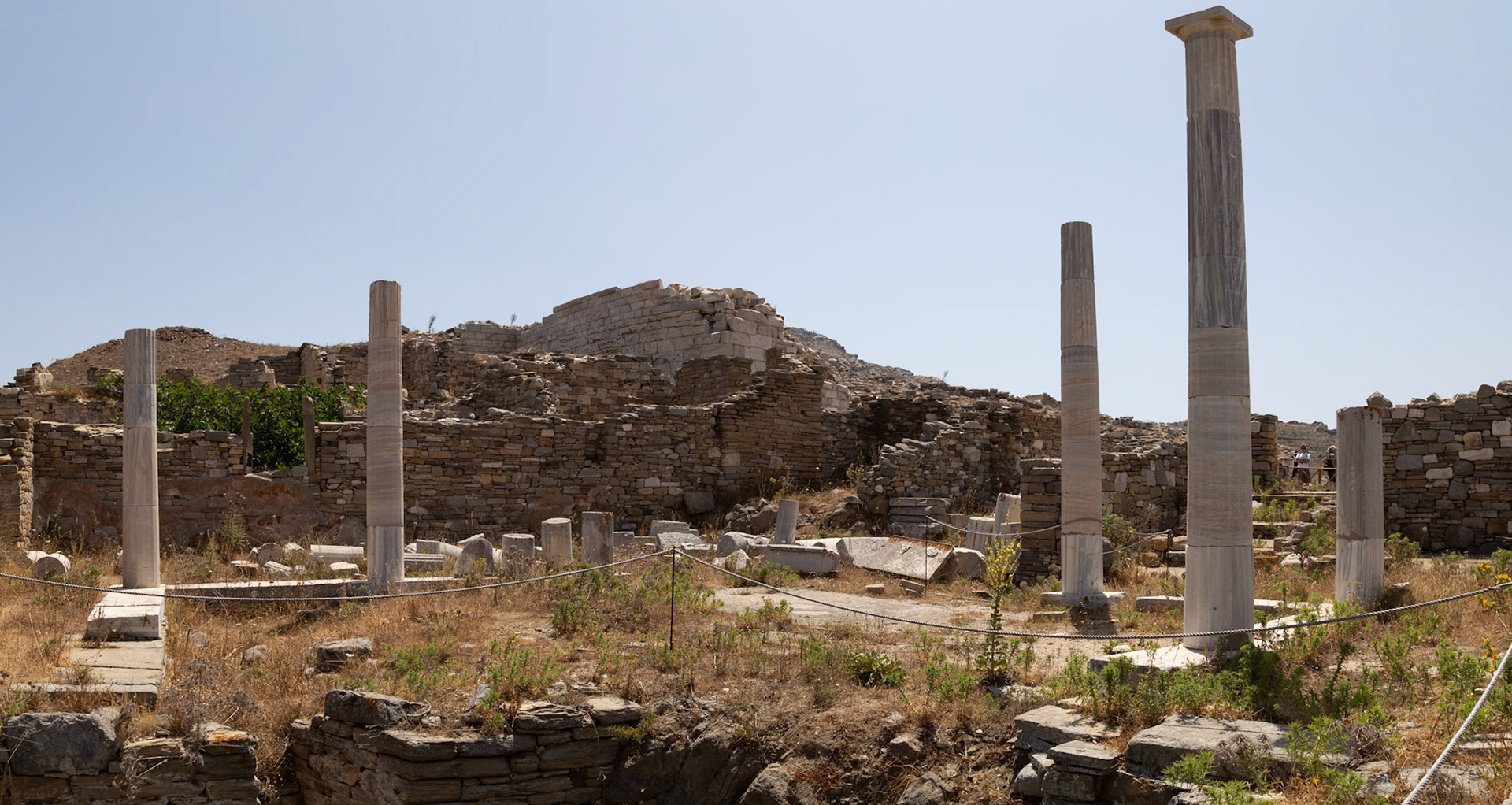 Delos, Greece - May 22nd 2018: Ancient ruins and standing columns are roped off to protect them from tourists visiting the archeological site.