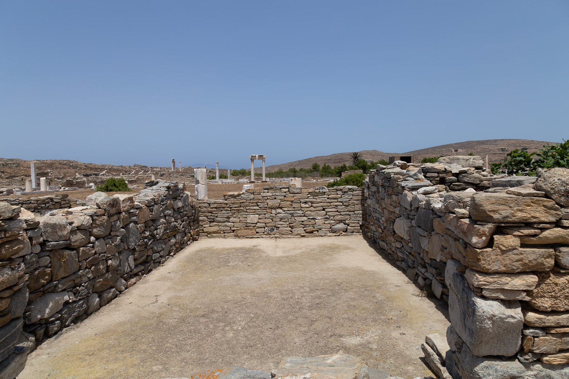 Delos, Greece - May 22nd 2018: Stone walls enclose an open space, part of the ancient ruins. This is likely a residential area, showcasing the architecture of the time.