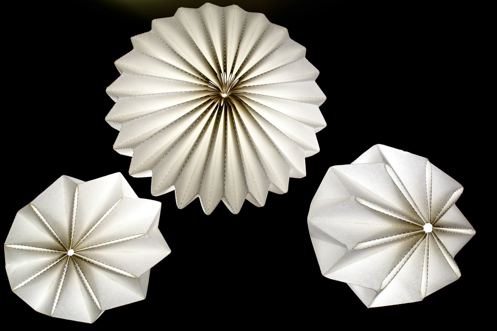 Three white paper rosettes are displayed against a black background, creating a decorative and artistic composition.