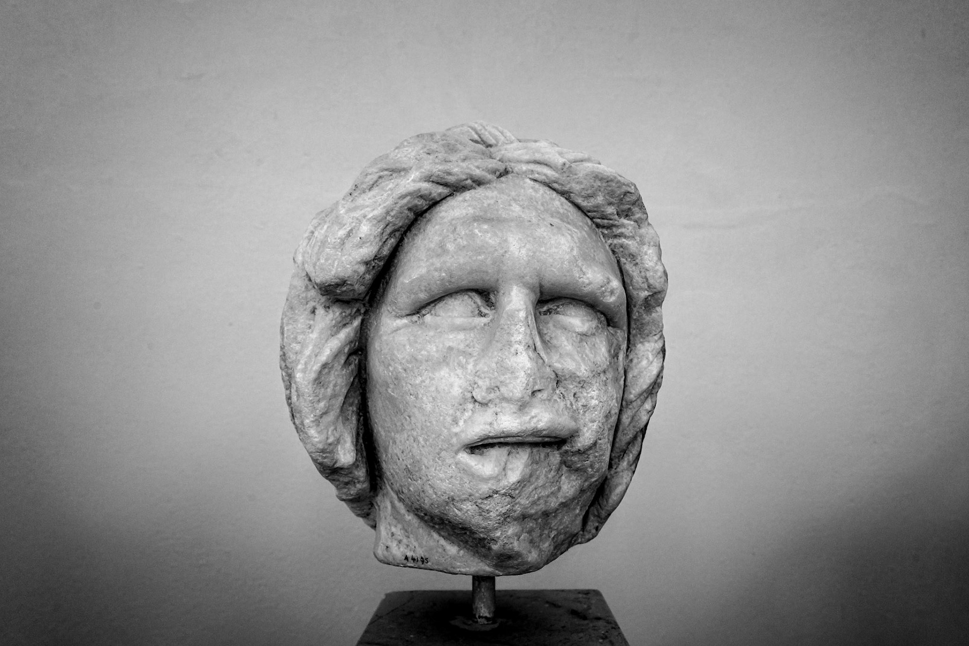 Delos, Greece - May 22nd 2018: A black and white shot of a marble head sculpture on display. The head is weathered, showing signs of age and wear.