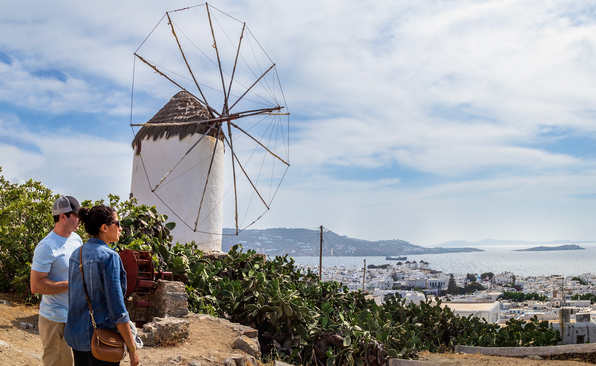 Mykonos, Greece - May 22nd 2018: Tourists admire a traditional windmill overlooking the town. These windmills were used to grind grain.