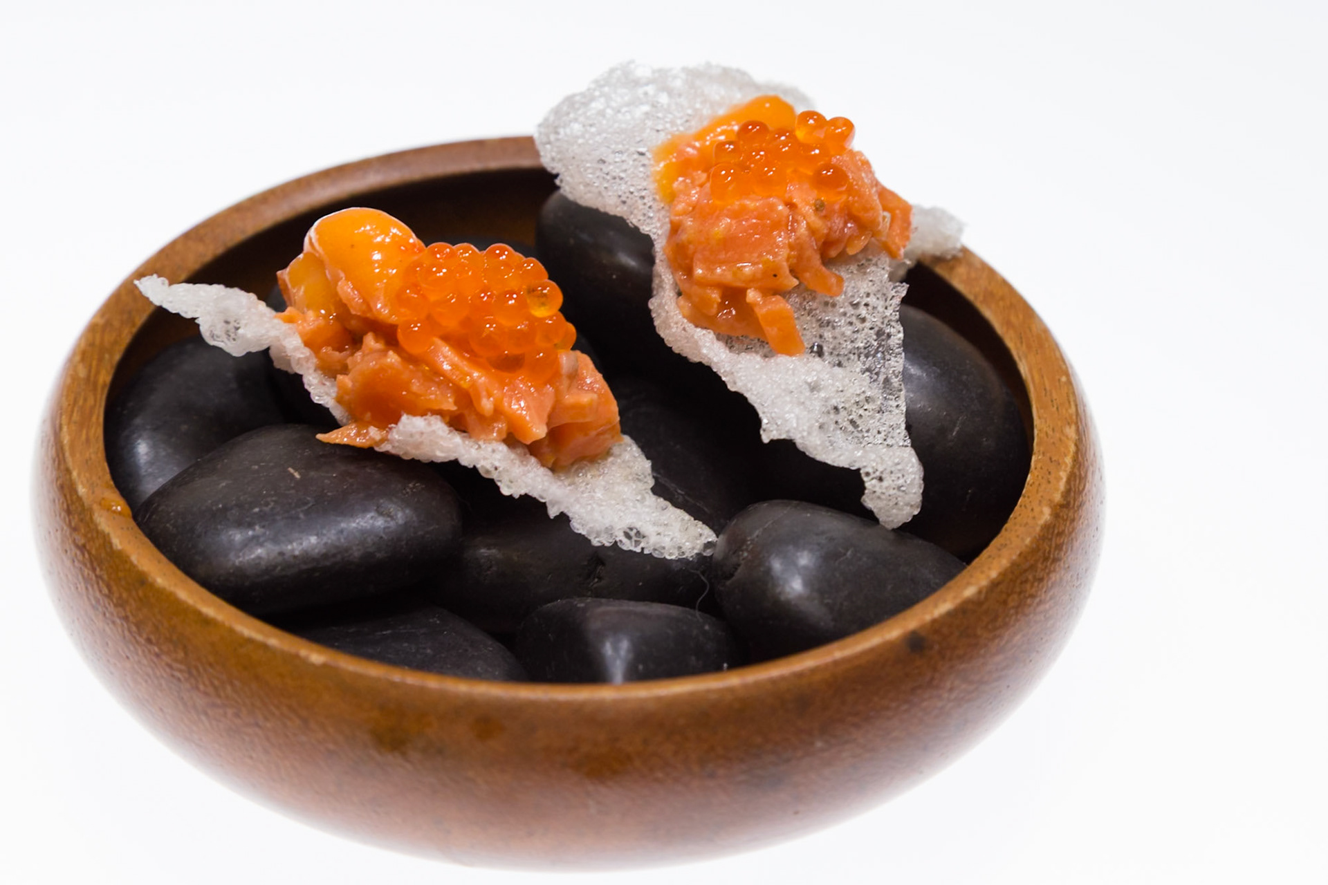 Fog Lark, Portland, Oregon - April 6th 2018: A culinary creation featuring salmon and roe atop a crispy base, presented in a wooden bowl with stones.