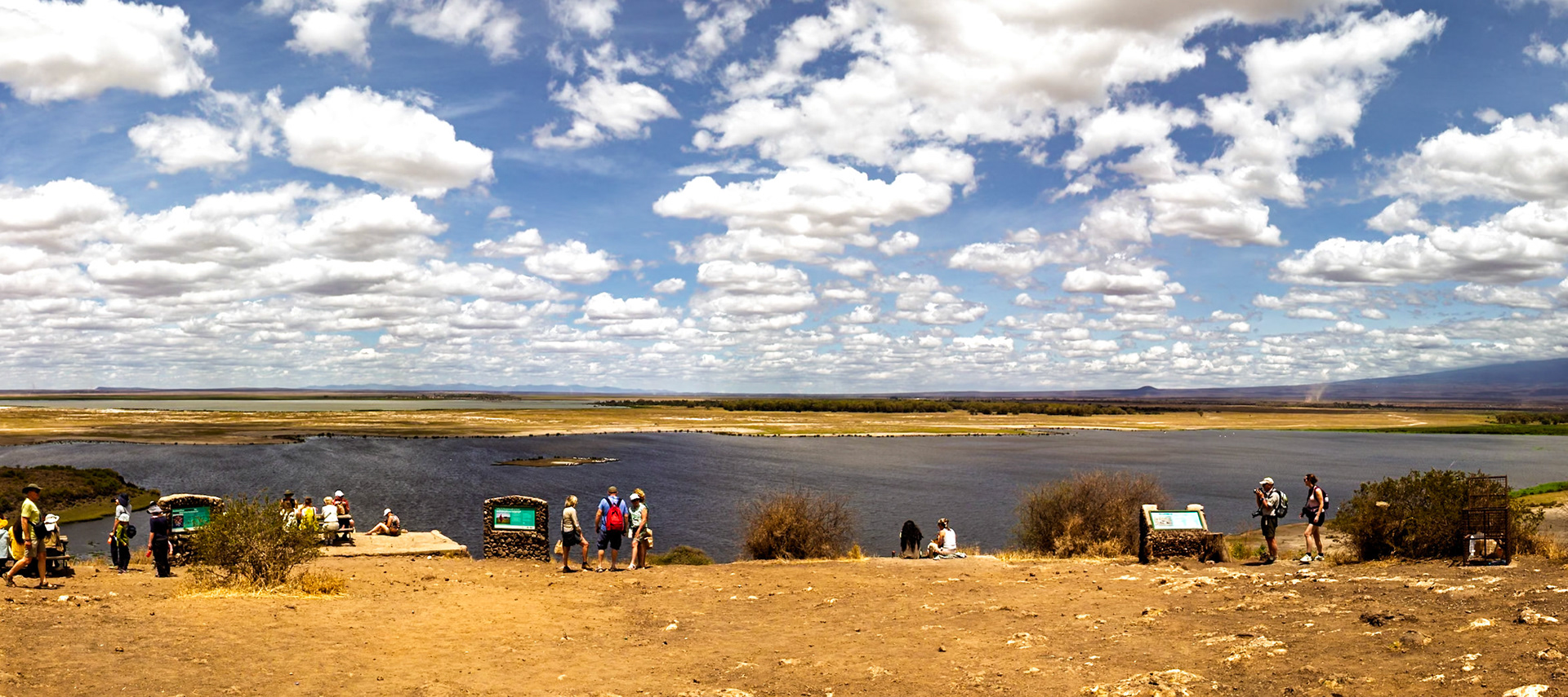 Tourists at Amboseli National Park in Kenya enjoy the view of the lake and landscape, learning about the area from informational signs.