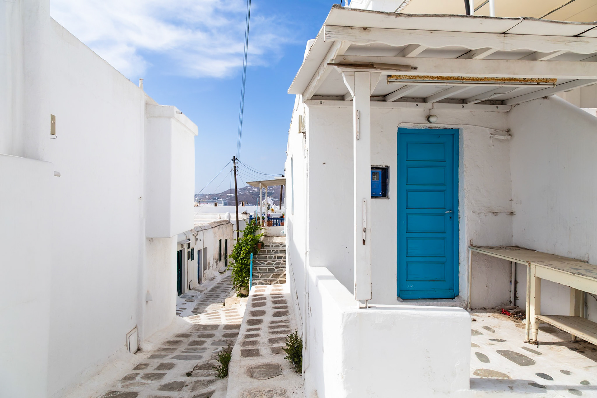 Mykonos, Greece - May 22nd 2018: A narrow street with white buildings and a blue door, showcasing the typical architecture of the island.