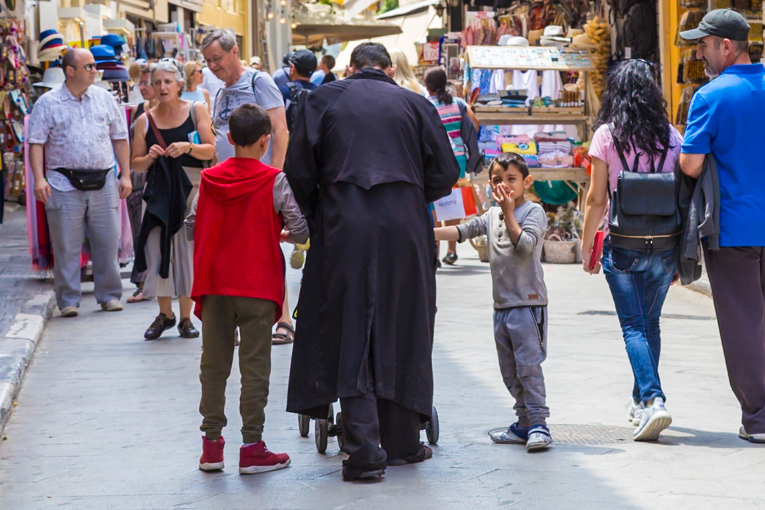 Athens, Greece - May 23rd 2018: A Greek Orthodox priest walks down a busy street with two young boys, likely engaging in conversation or a religious lesson.