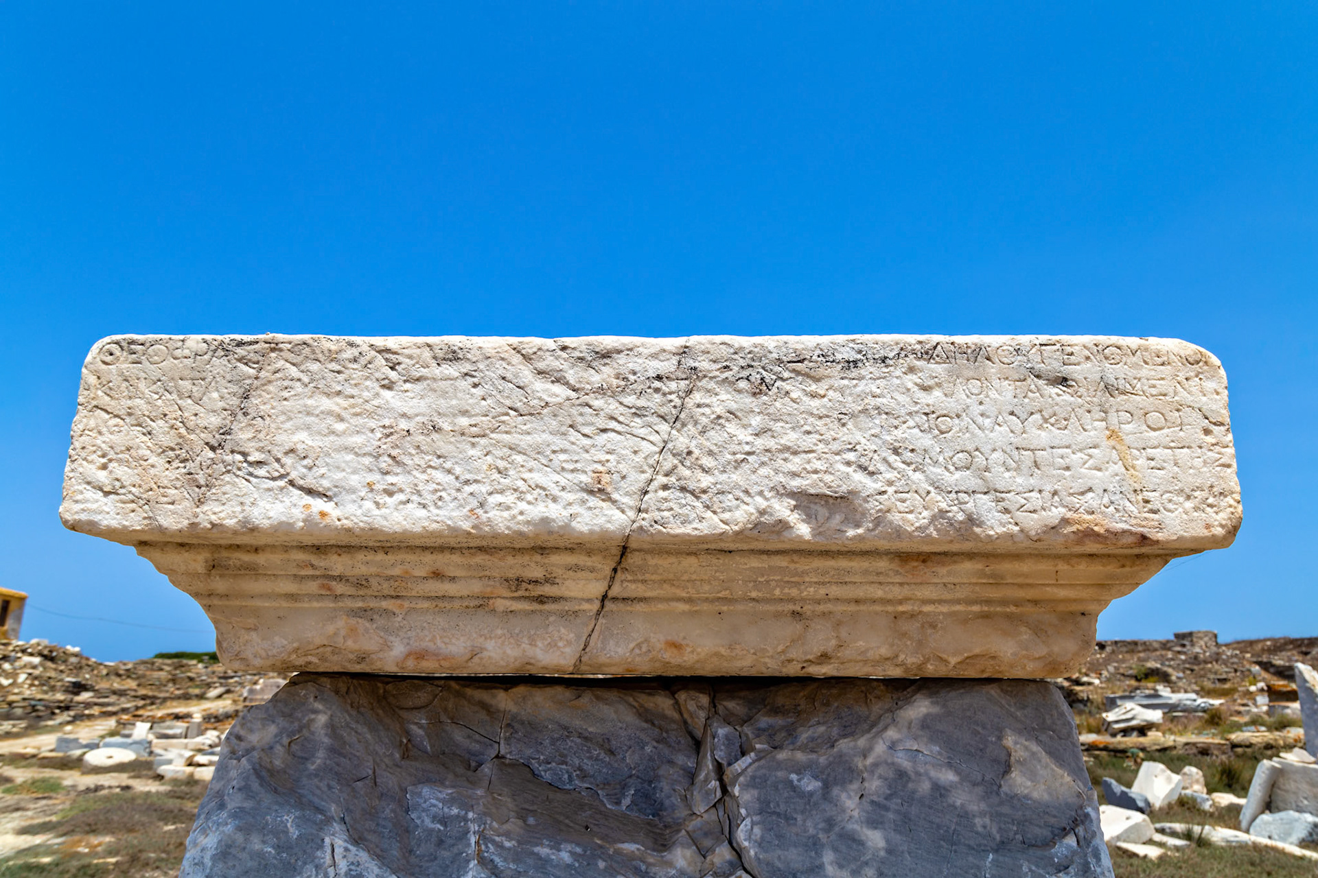 Delos, Greece - May 22nd 2018: A marble block with ancient Greek inscriptions sits atop another stone, part of the ruins on the island of Delos, a UNESCO World Heritage site.
