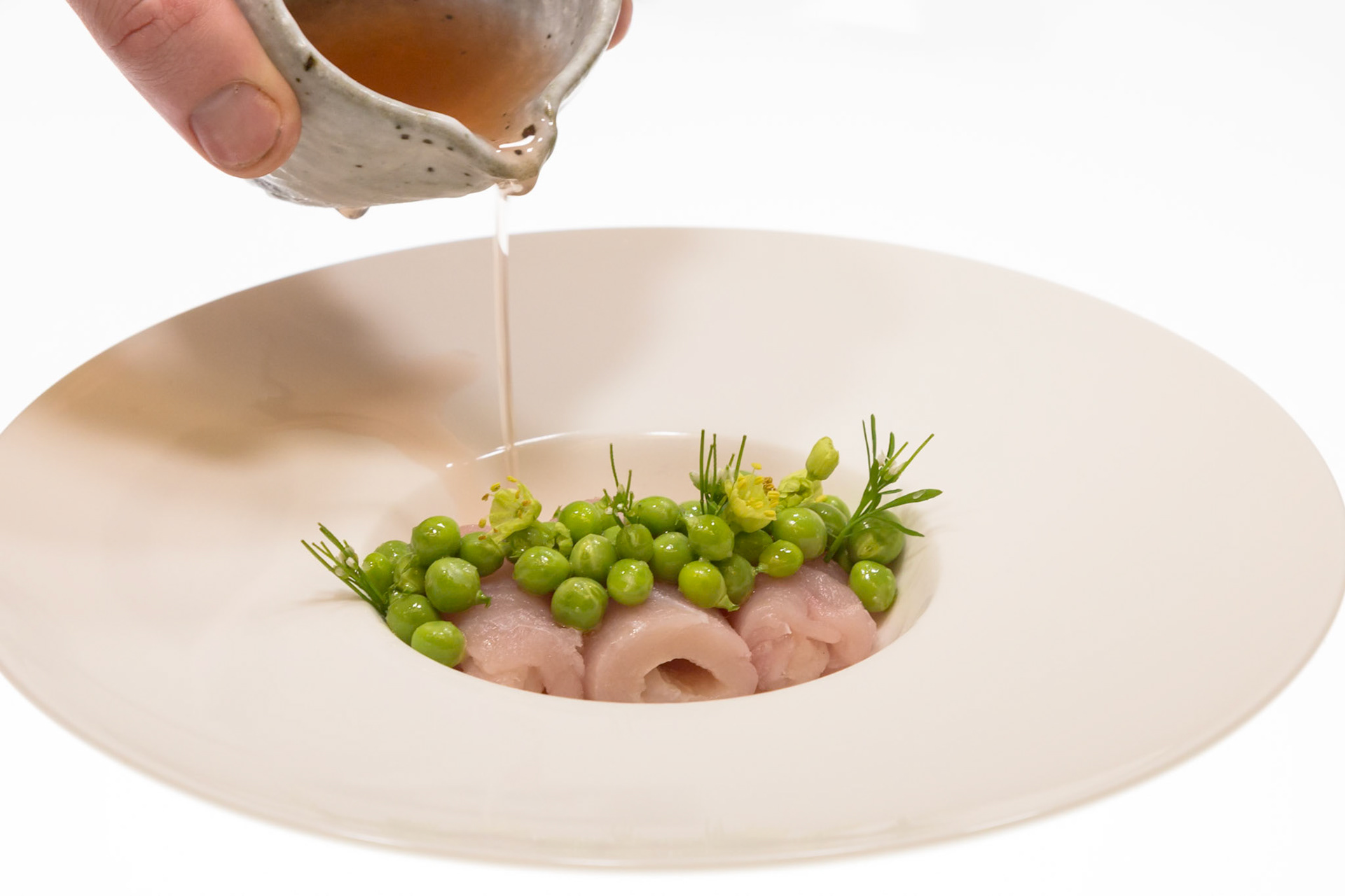 Fog Lark, Portland, Oregon - April 6th 2018: A chef pours broth over a dish of fish, peas, and herbs, enhancing its flavor and presentation.
