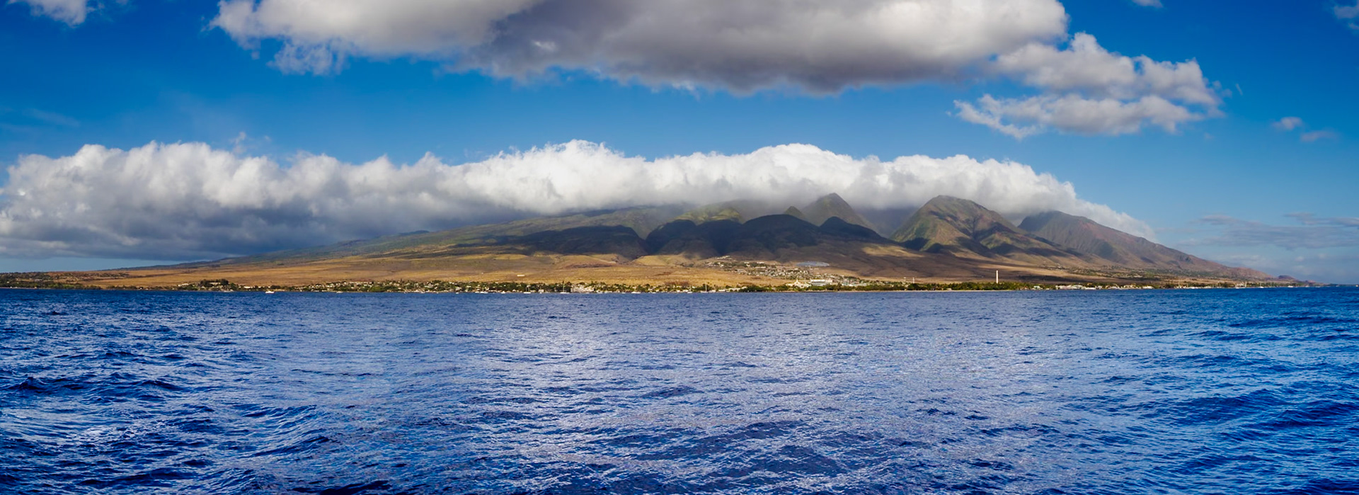 Maui, Hawaii, USA - April 7th 2022: A scenic view of the island from the ocean, with clouds hovering over the mountain range.