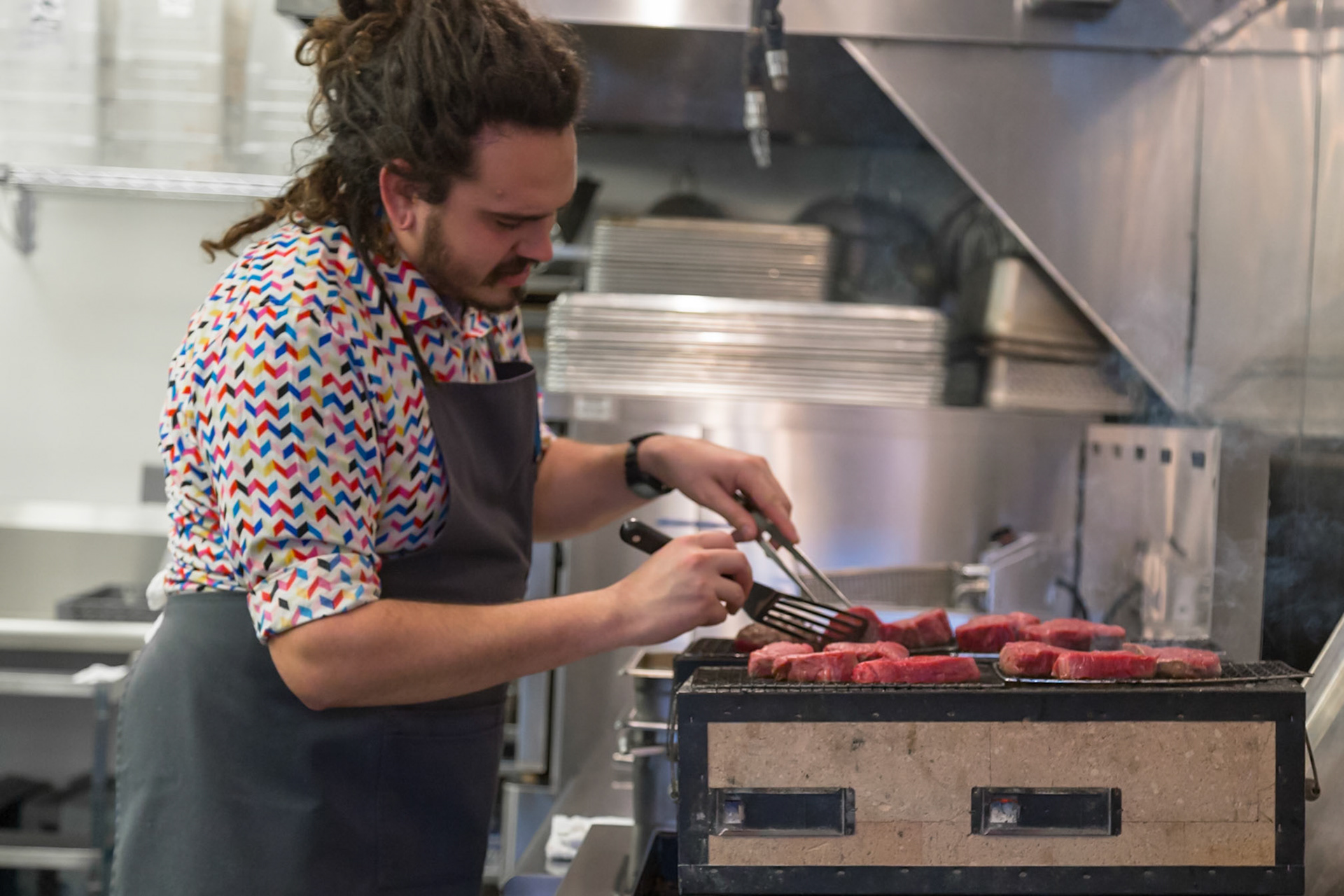 Fog Lark, Portland, Oregon - April 6th 2018: A chef grills steaks in a restaurant kitchen, using tongs to turn the meat.