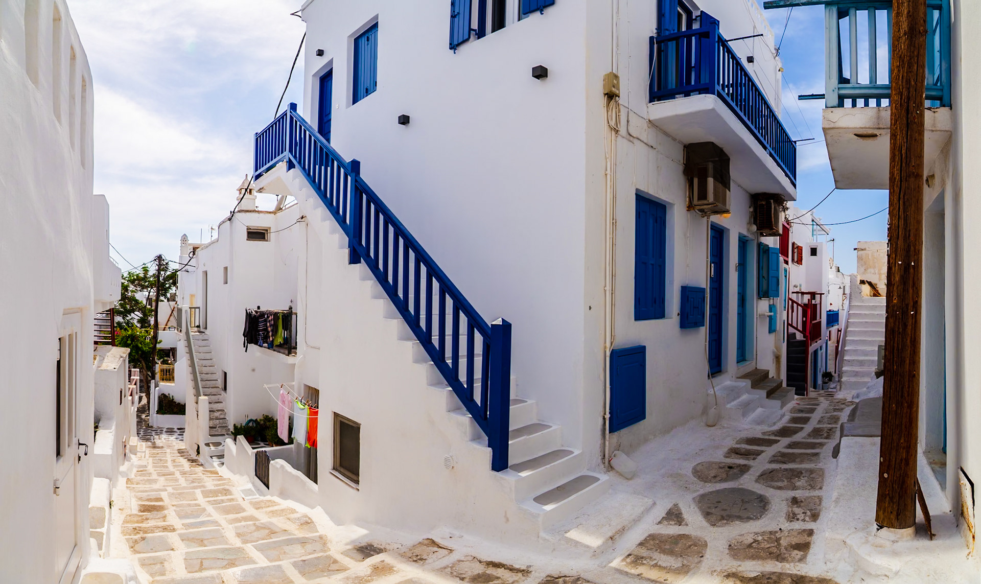 Mykonos, Greece - May 22nd 2018: A typical street scene in Mykonos, featuring white buildings with blue accents and cobblestone streets.