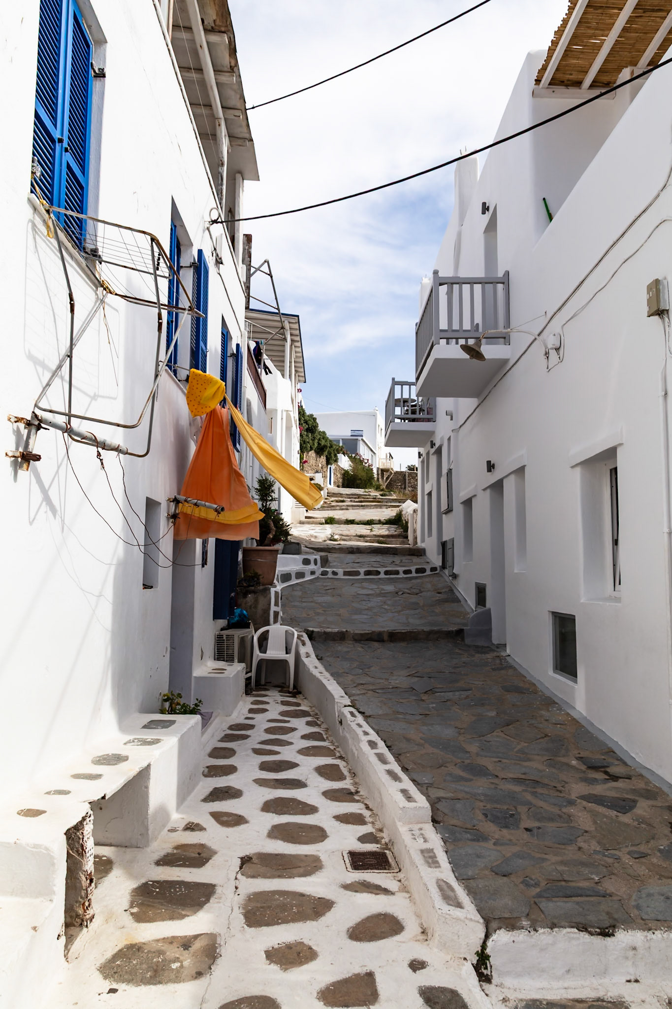 Mykonos, Greece - May 22nd 2018: A narrow street with white buildings and blue shutters leads uphill, showcasing the island's traditional architecture.