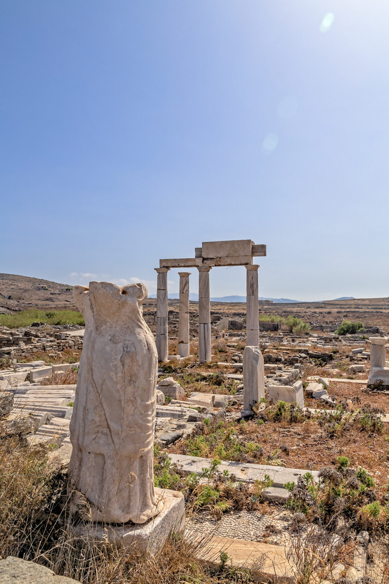 Delos, Greece - May 22nd 2018: Ruins of the ancient city of Delos, including the headless statue of a woman and the remains of a temple, stand as a testament to its rich history.