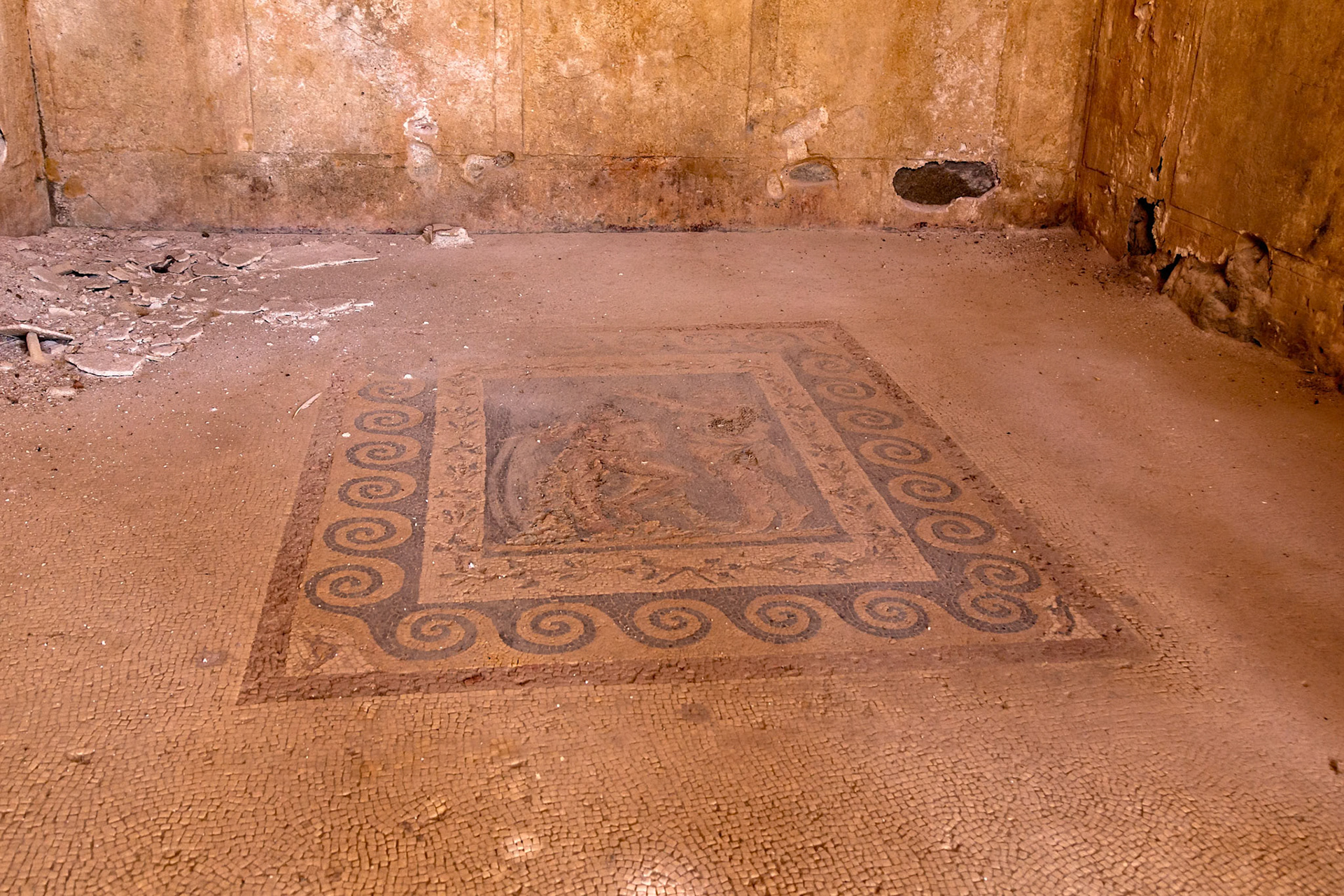 Delos, Greece - May 22nd 2018: An ancient mosaic floor is seen in a room on the island of Delos. The mosaic is decorated with a spiral pattern and a central image.