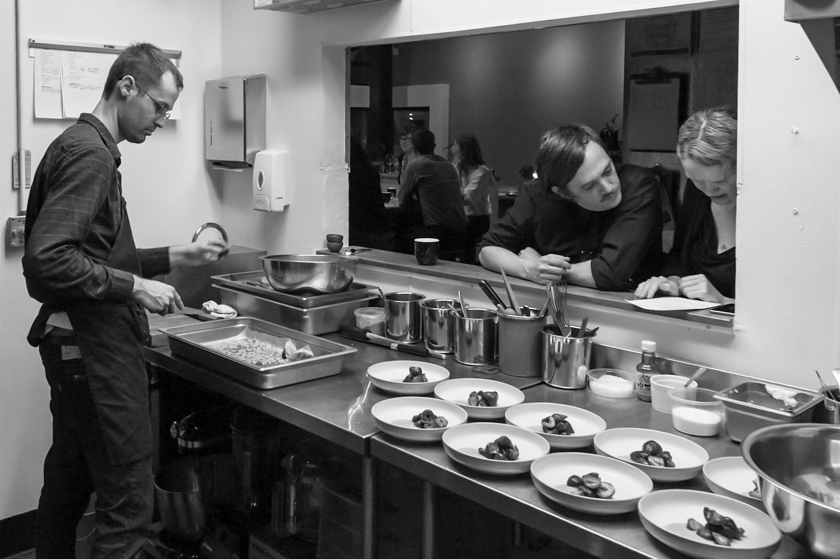 Fog Lark, Portland, Oregon - April 6th 2018: A chef plates desserts while two others look on from the dining area, likely ensuring quality control.