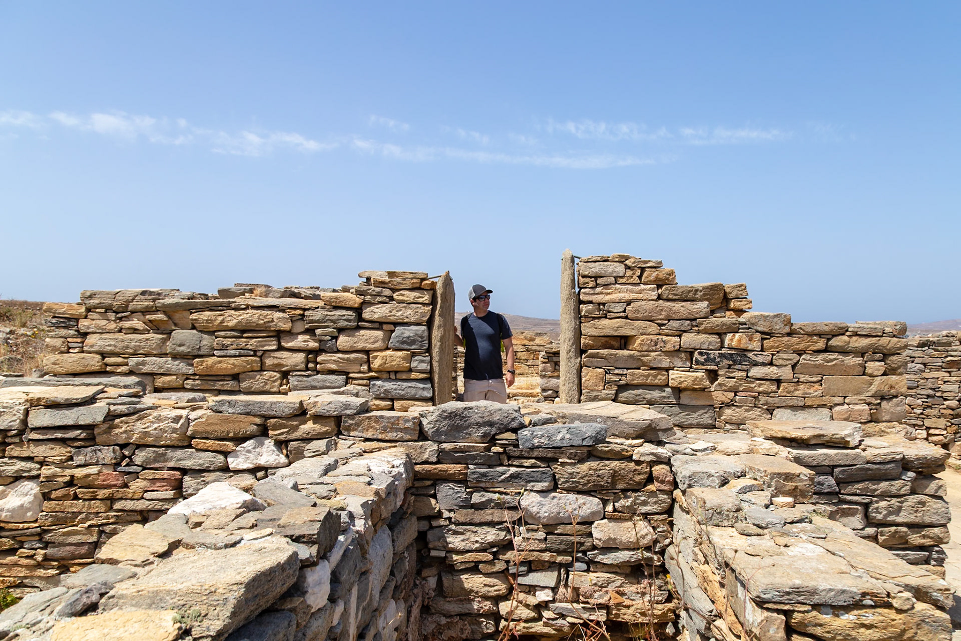 Delos, Greece - May 22nd 2018: A man explores the ancient ruins of Delos, Greece, walking through a stone doorway, taking in the historical site.