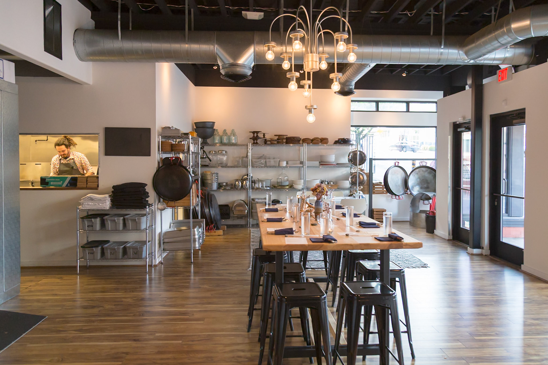 Fog Lark, Portland, Oregon - April 6th 2018: A chef prepares for a dinner service in a well-lit restaurant with a long table set for guests.
