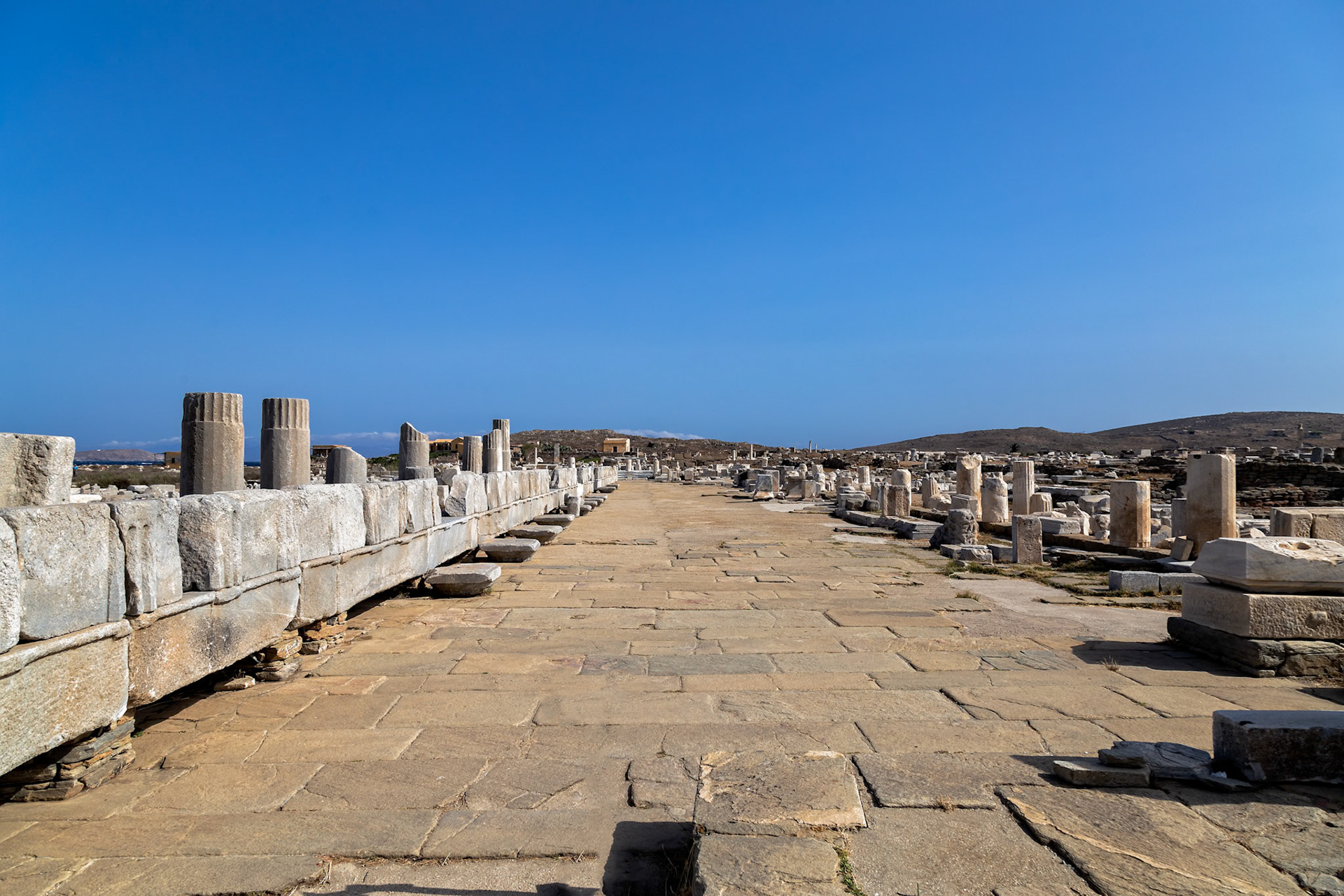 Delos, Greece - May 22nd 2018: Ruins of an ancient city are seen, with stone structures and columns lining a path. This is a historical site for tourists to explore.