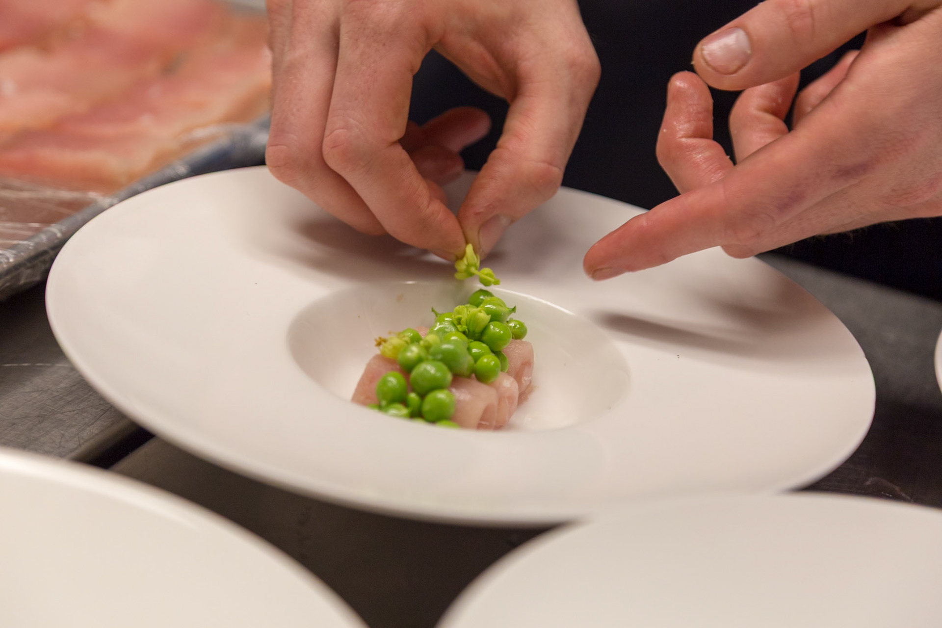 Fog Lark, Portland, Oregon - April 6th 2018: A chef delicately plates a dish with fish, peas, and pea shoots for a refined dining experience.