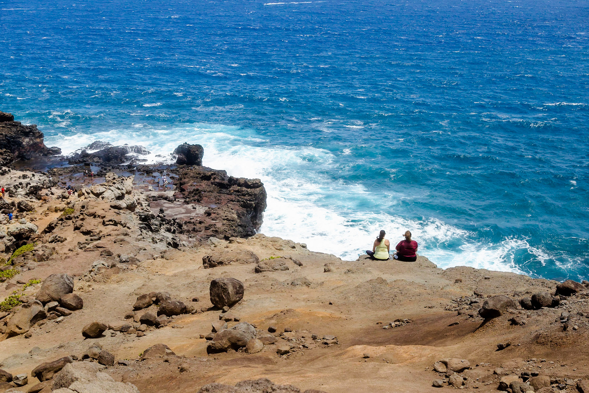 Maui, Hawaii, USA - April 9th 2022: Two women sit on a cliff overlooking the ocean, enjoying the view and the sound of the waves crashing.
