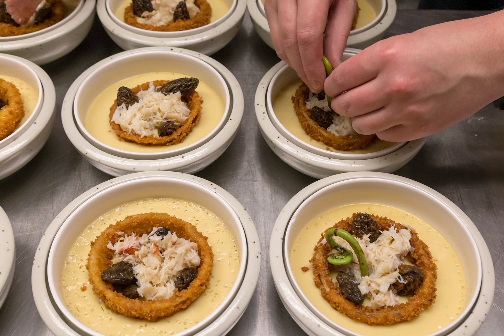 Fog Lark, Portland, Oregon - April 6th 2018: A chef plates a dish with crab, morels, and a fried onion ring in a custard base for service.