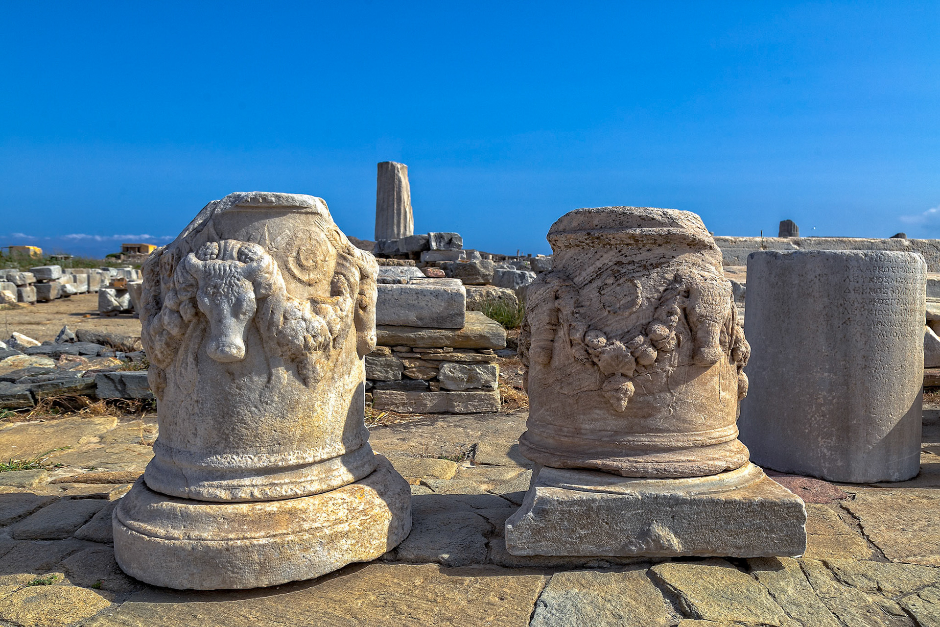 Delos, Greece - May 22nd 2018: Ancient ruins are preserved on Delos, a Greek island. The image shows carved stone columns and a clear blue sky.