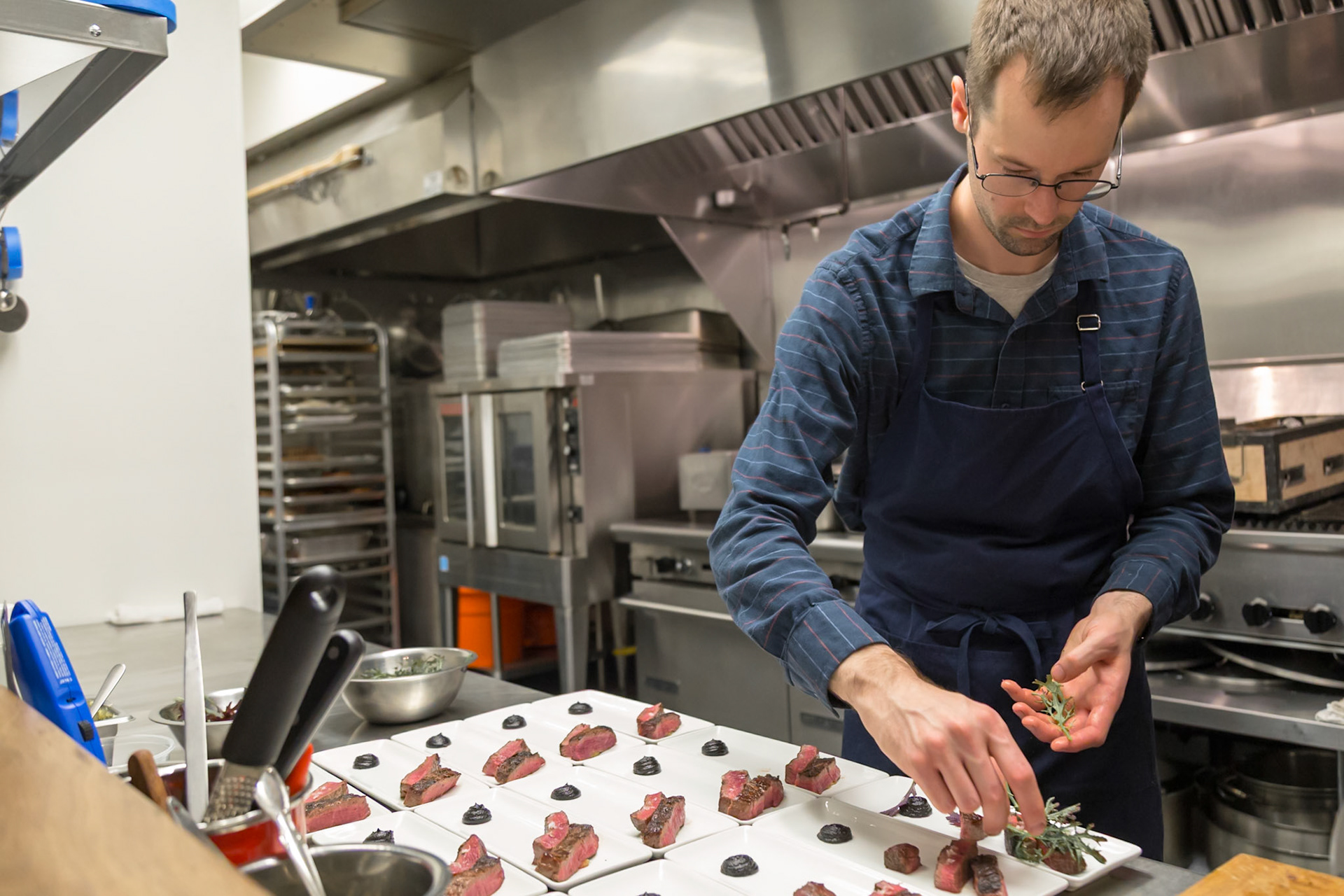 Fog Lark, Portland, Oregon - April 6th 2018: A chef plates steak appetizers with herbs in a professional kitchen, preparing for an event.