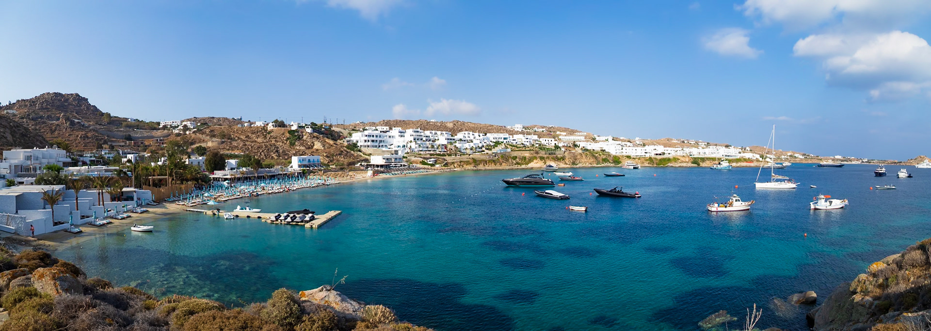 Psarou Beach, Mykonos, Greece - May 24th 2018: A scenic view of the beach with boats in the water and people enjoying the sun and sand.