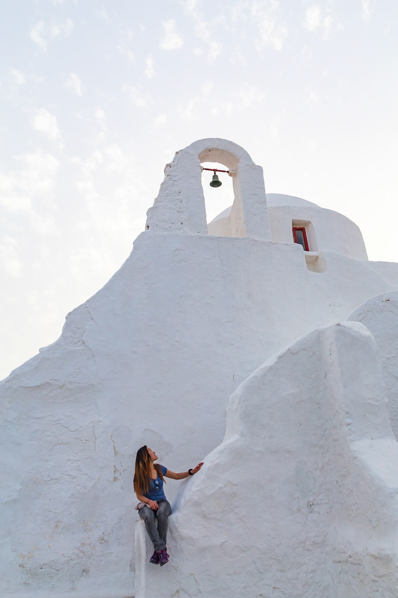 Mykonos, Greece - May 23rd 2018: A tourist admires the iconic whitewashed architecture and bell tower of a traditional Greek Orthodox church.