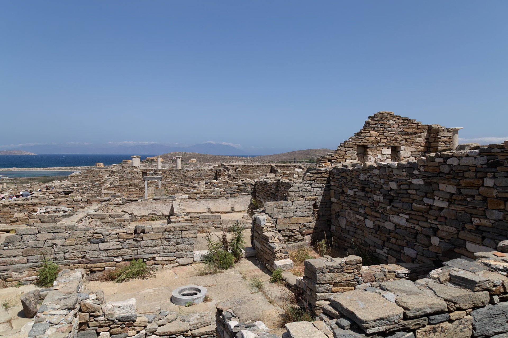 Delos, Greece - May 22nd 2018: Ruins of ancient buildings stand on Delos, a Greek island and archaeological site. Tourists explore the historical site.