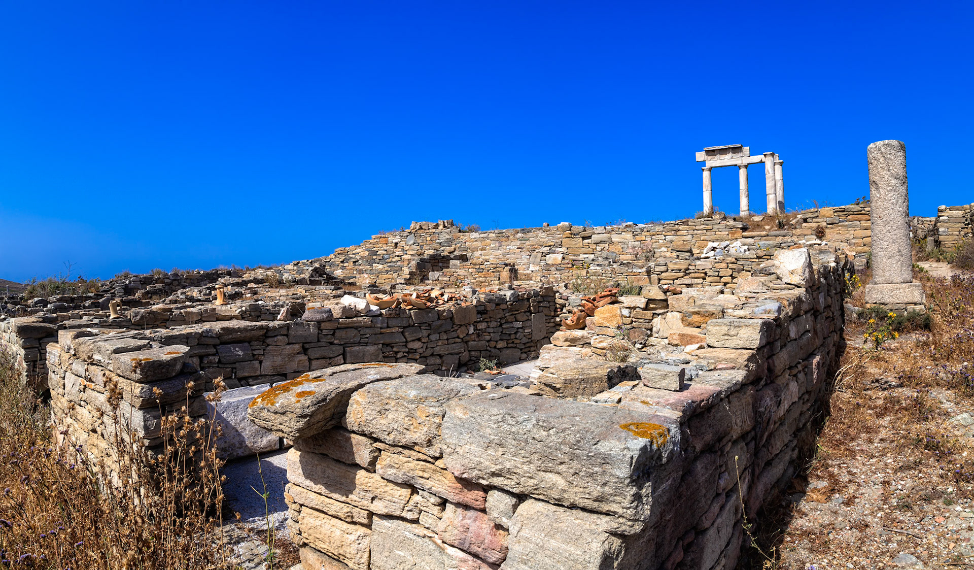 Delos, Greece - May 22nd 2018: Ancient ruins stand against a clear blue sky. The stone structures, remnants of a bygone era, evoke a sense of history and wonder.