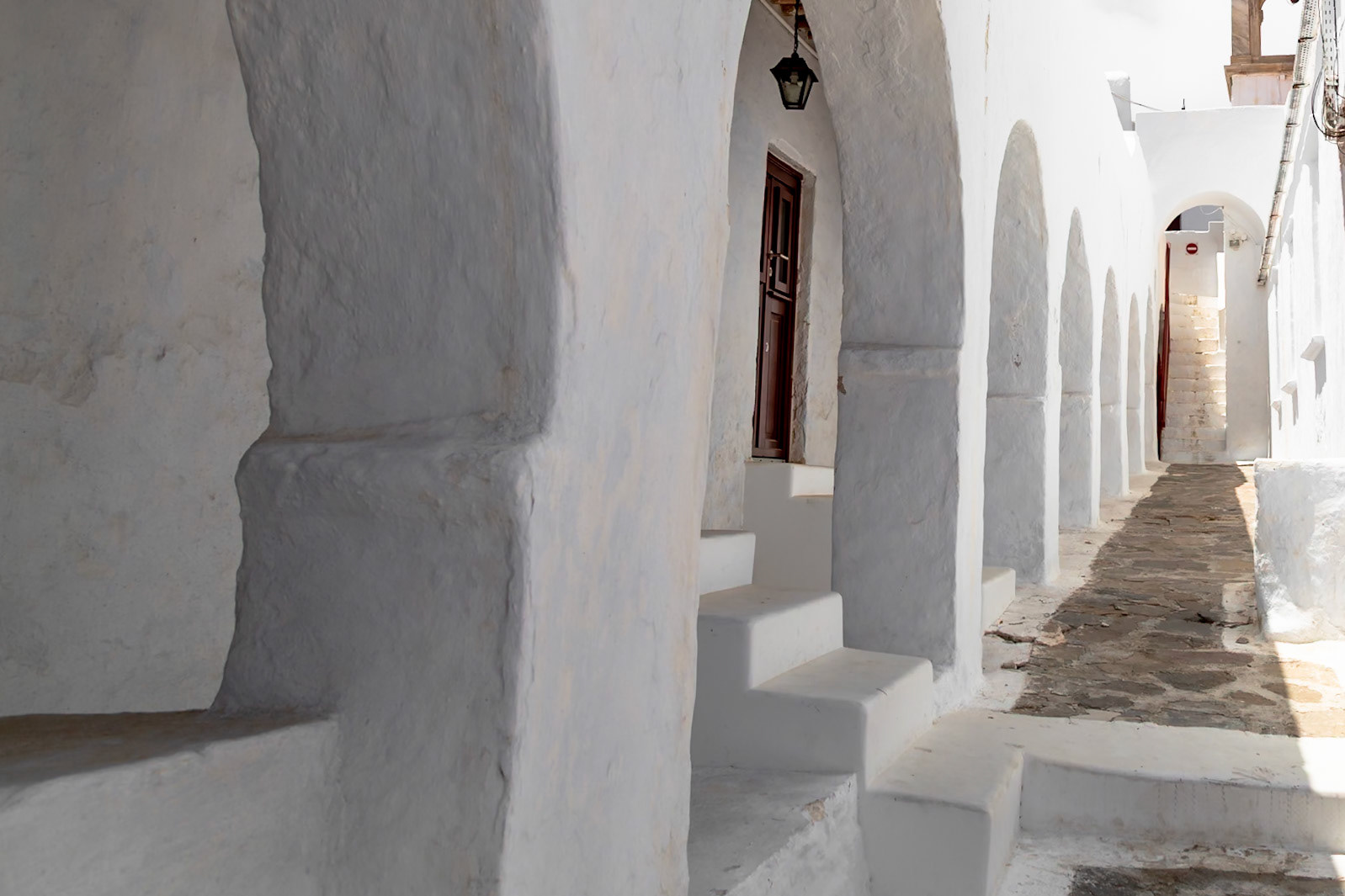 Mykonos, Greece - May 22nd 2018: A narrow, stone-paved street lined with white buildings and archways, showcasing the island's unique architecture.