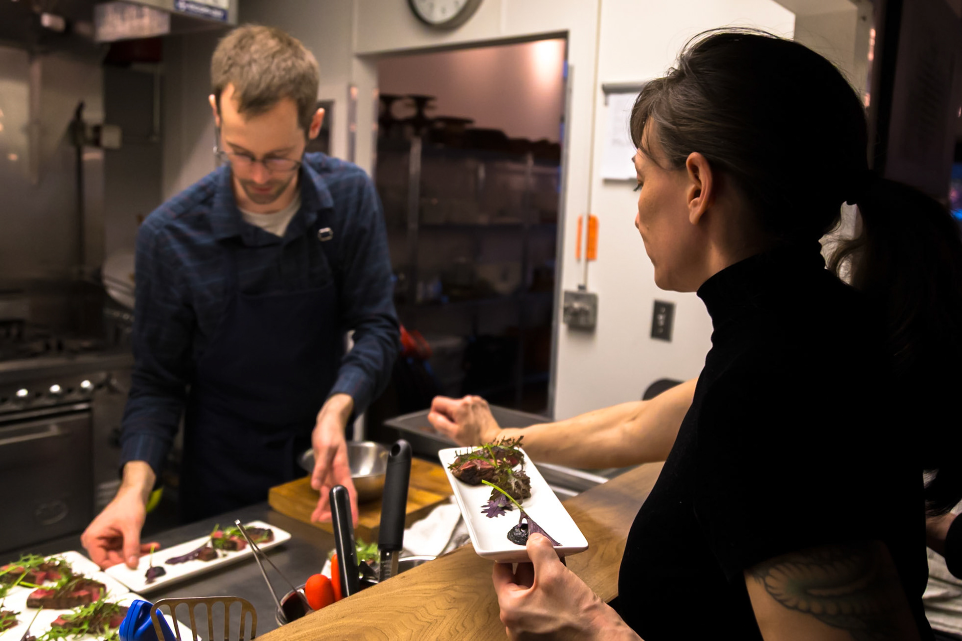 Fog Lark, Portland, Oregon - April 6th 2018: A chef plates a dish as a server waits to deliver it to a customer.