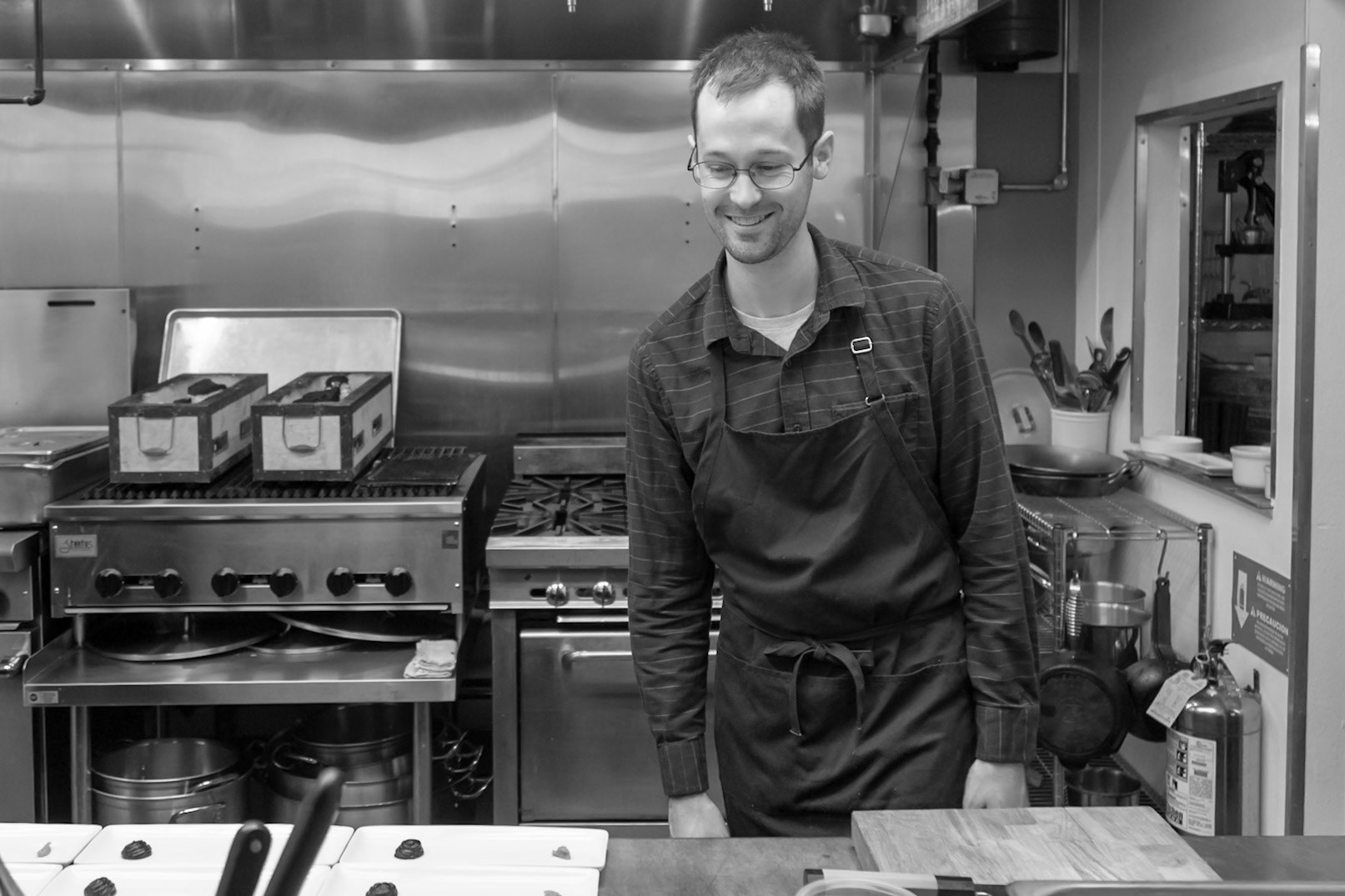 Fog Lark, Portland, Oregon - April 6th 2018: A chef smiles in a professional kitchen, possibly inspecting plated dishes before service.