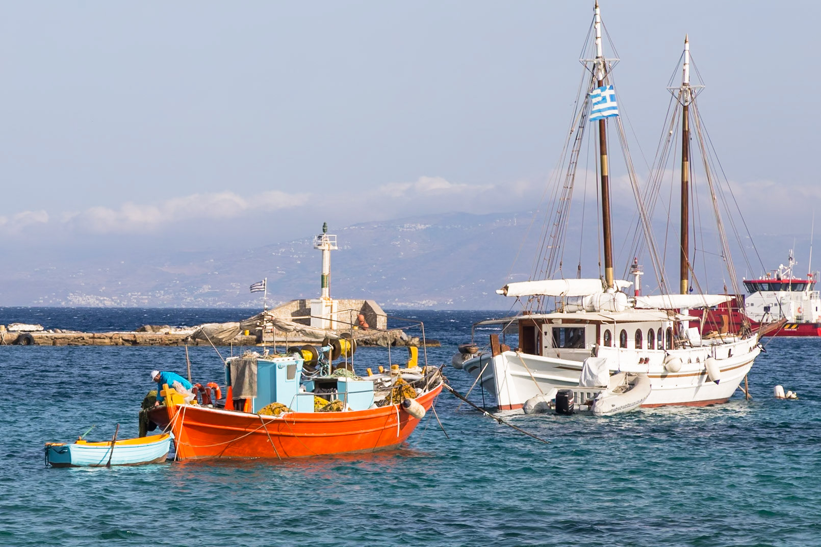 Mykonos, Greece - May 23rd 2018: Fishing boats bob in the harbor, their vibrant colors contrasting with the whitewashed buildings in the background.