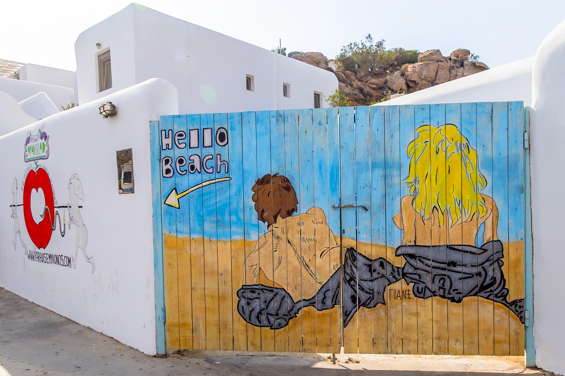 Paradise Beach, Mykonos, Greece - May 24th 2018: A painted gate welcomes visitors with a "Hello Beach" sign and playful beachgoers art.