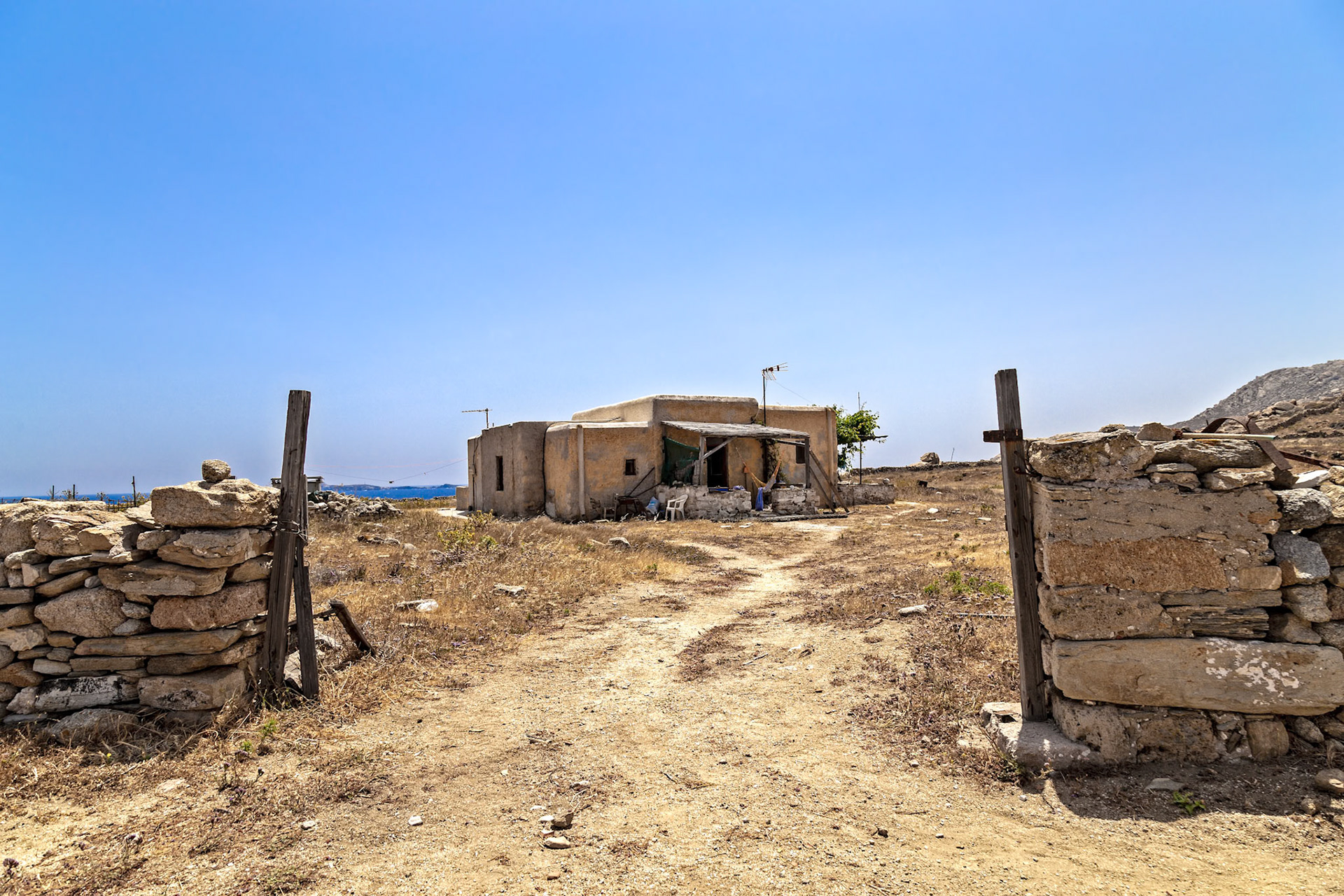 Delos, Greece - May 22nd 2018: A rustic house stands on Delos, framed by a stone gate. People relax on the porch, enjoying the tranquil Greek island life.