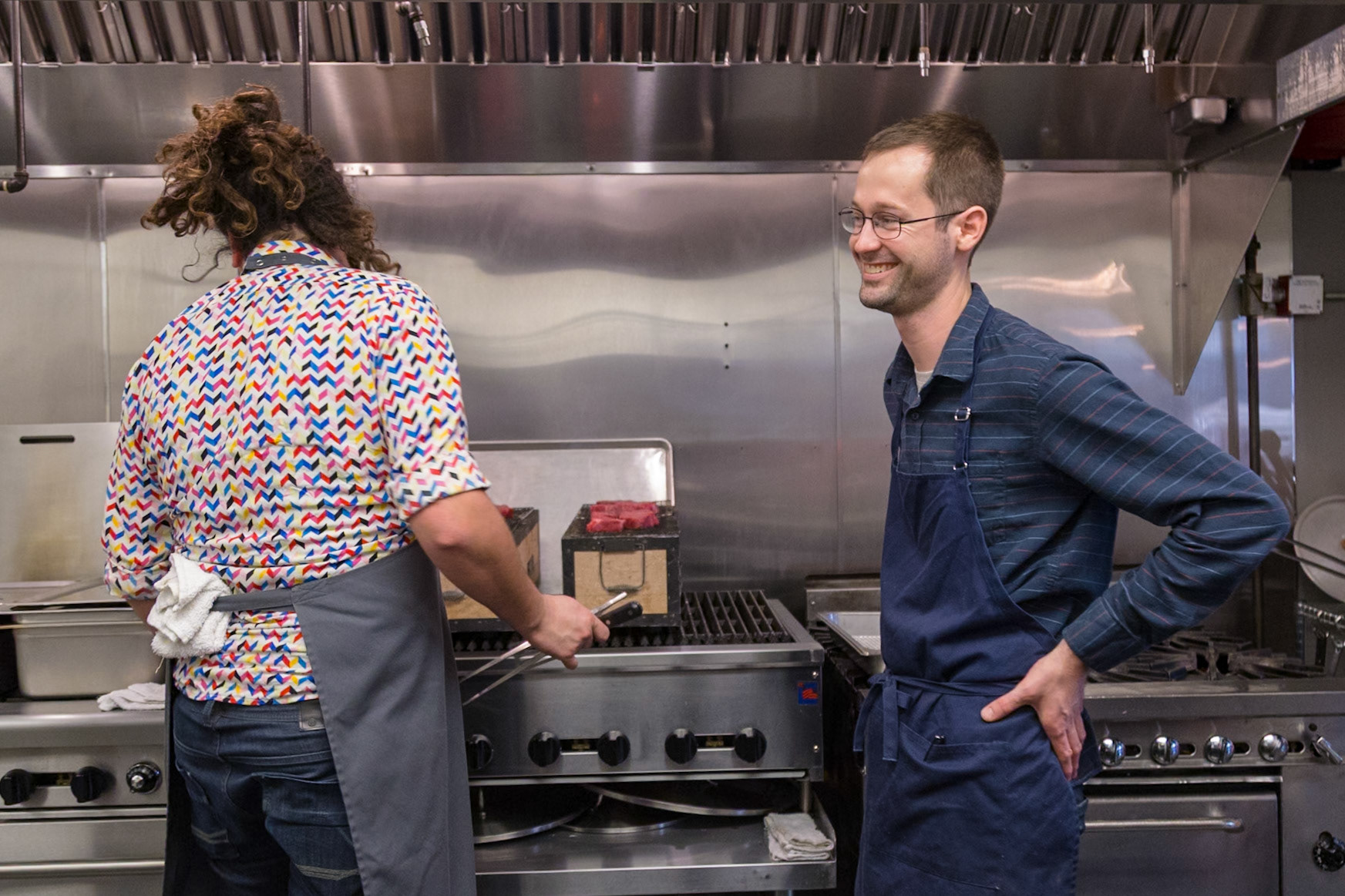 Fog Lark, Portland, Oregon - April 6th 2018: Two chefs in a restaurant kitchen, one grilling meat, the other watching with a smile.