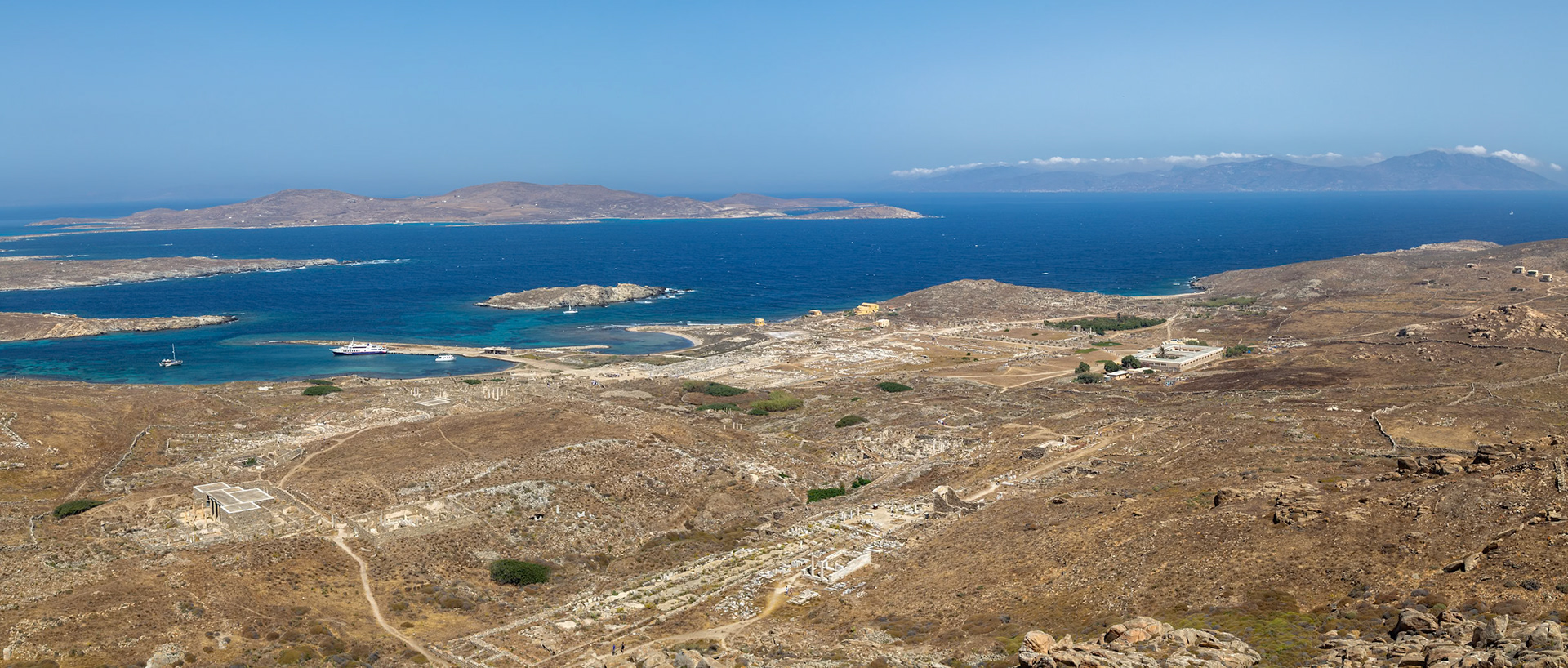 Delos, Greece - May 22nd 2018: A high-angle view shows the ancient ruins of Delos, a Greek island, with the Aegean Sea and other islands in the background, showcasing its historical significance.