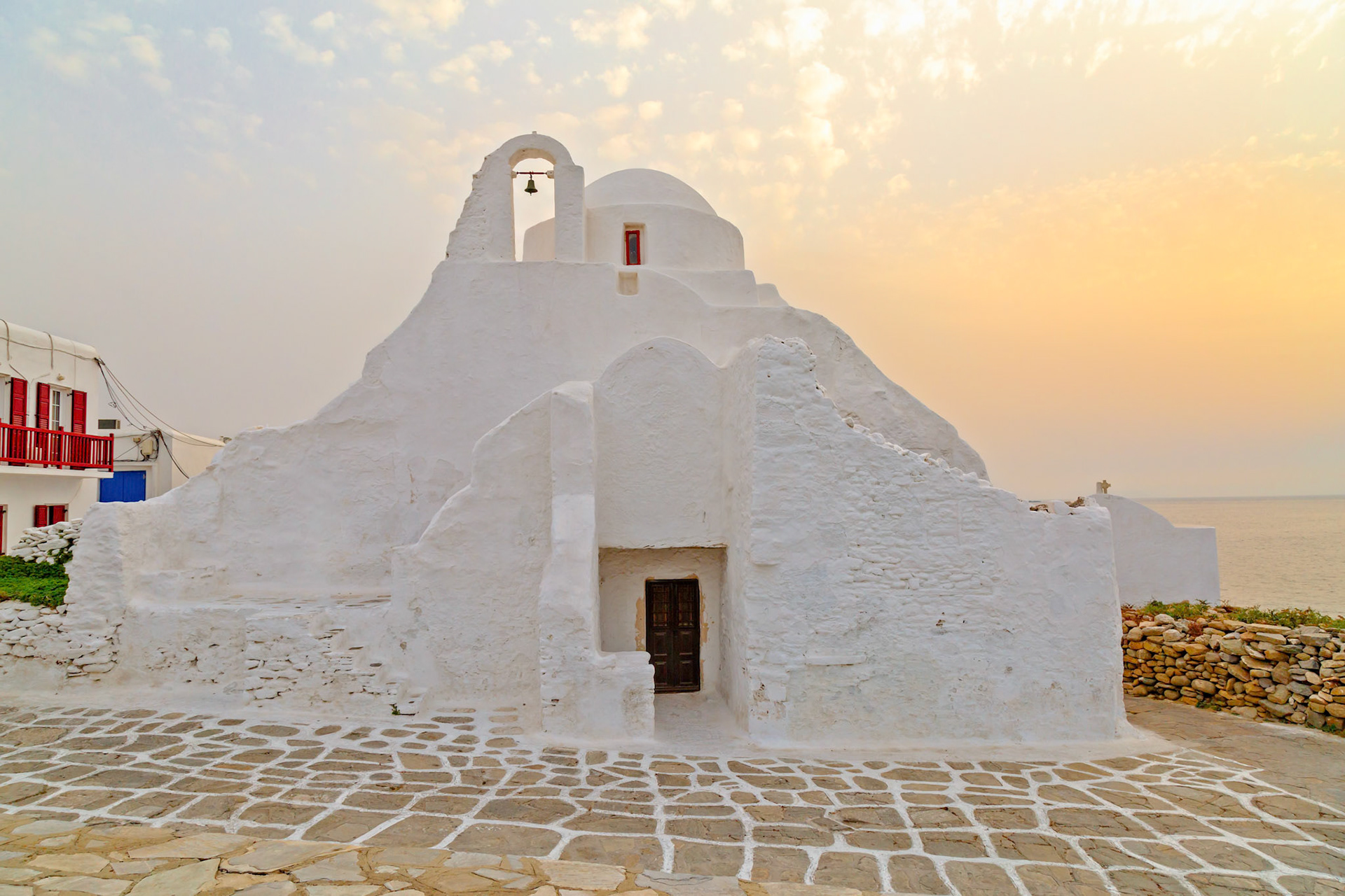 Mykonos, Greece - May 23rd 2018: The iconic whitewashed Paraportiani Church stands proudly against the Aegean Sea, a testament to Cycladic architecture.